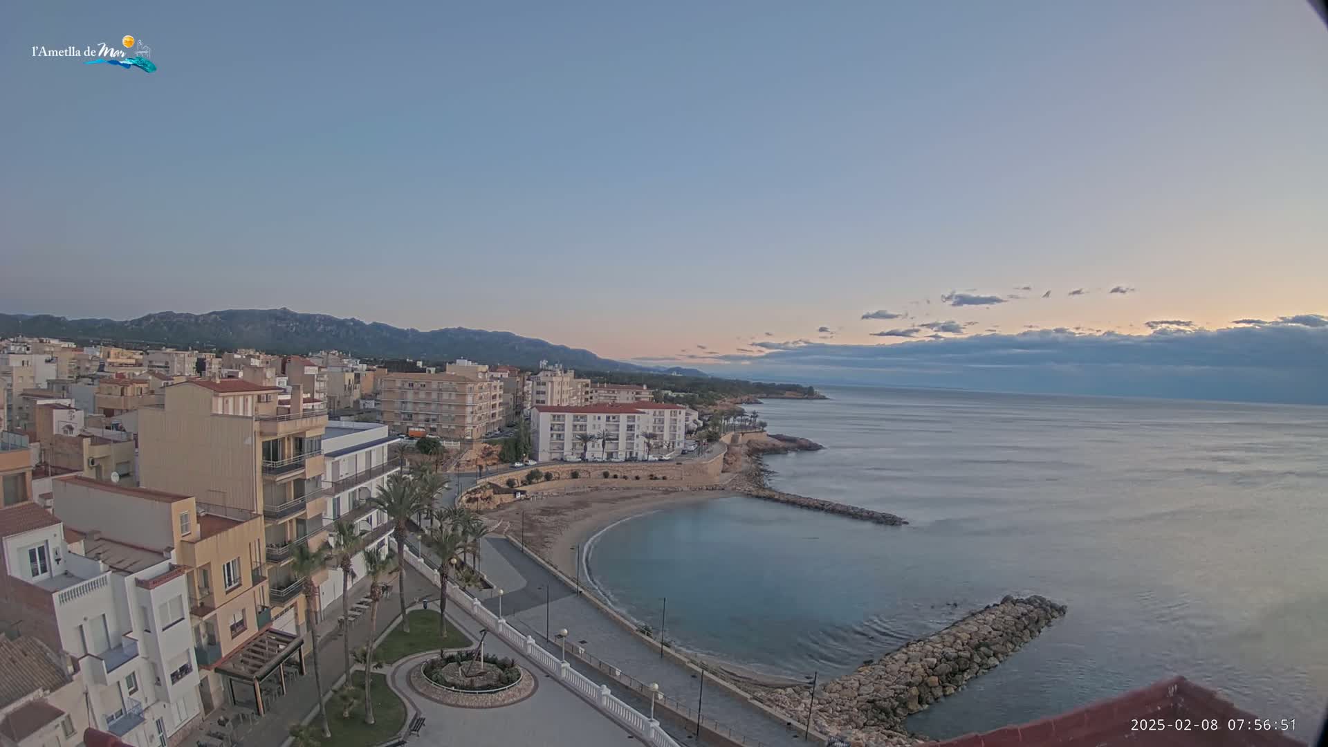 A coastal town with multi-story buildings, a small sandy cove, and a calm sea under a mostly clear, twilight sky.
