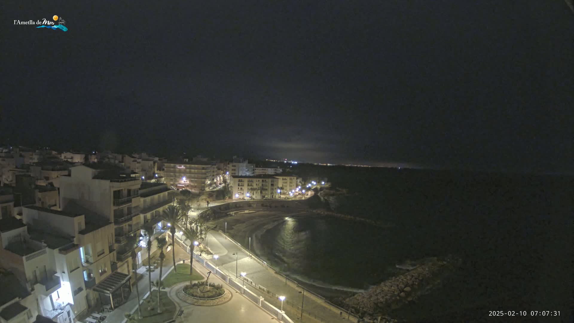 A nighttime view of a coastal town with a crescent-shaped bay, illuminated by streetlights.