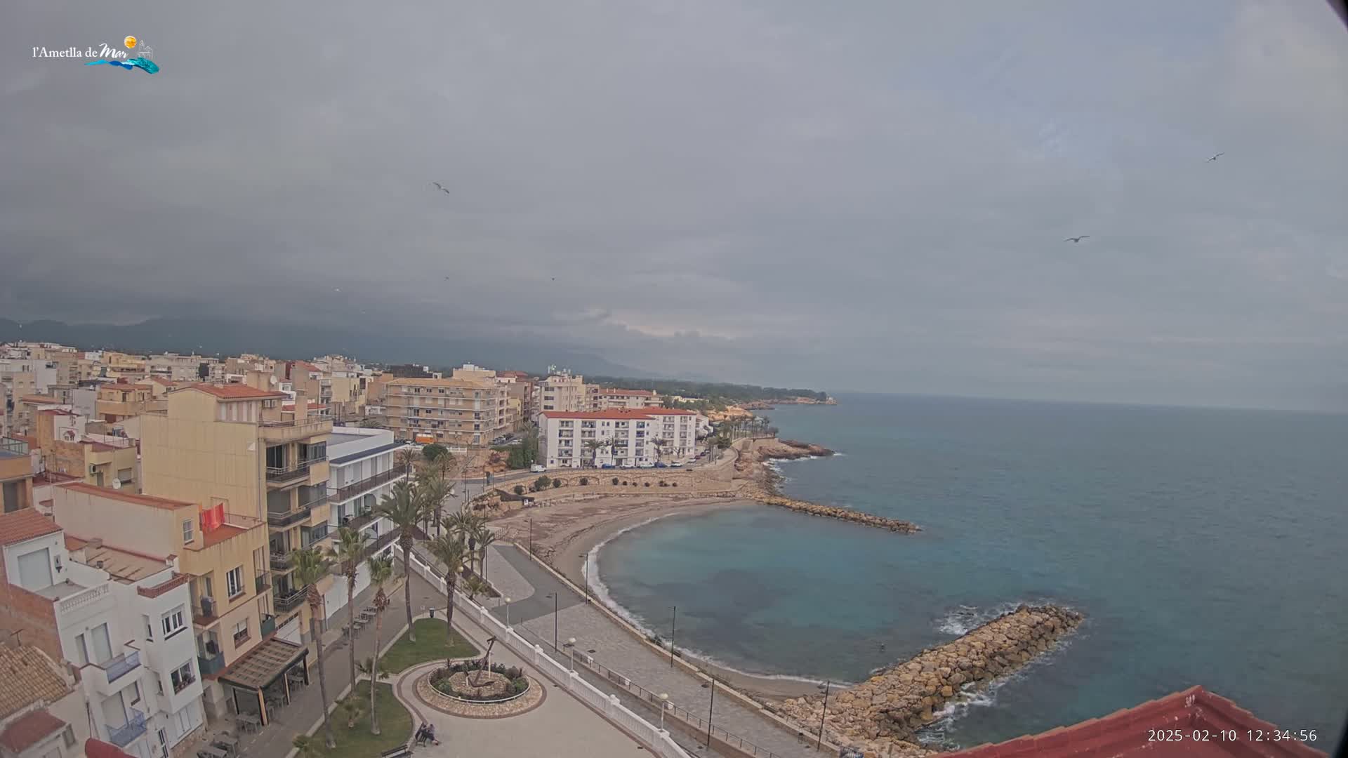 An overcast day reveals a coastal town with multi-story buildings and a small, sandy cove nestled between a rocky shoreline and the calm sea.
