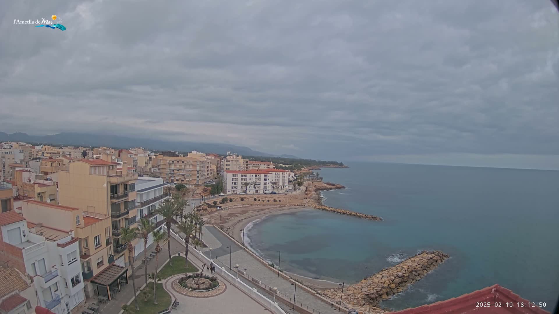 A coastal town with multi-story buildings and a small, sandy cove is visible under an overcast sky.