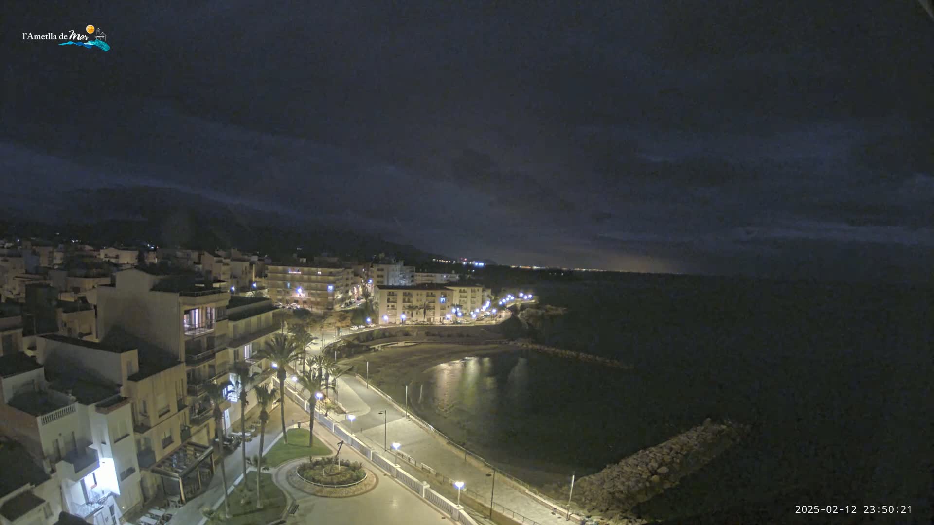 A nighttime coastal town with a calm bay is visible under a partly cloudy sky.