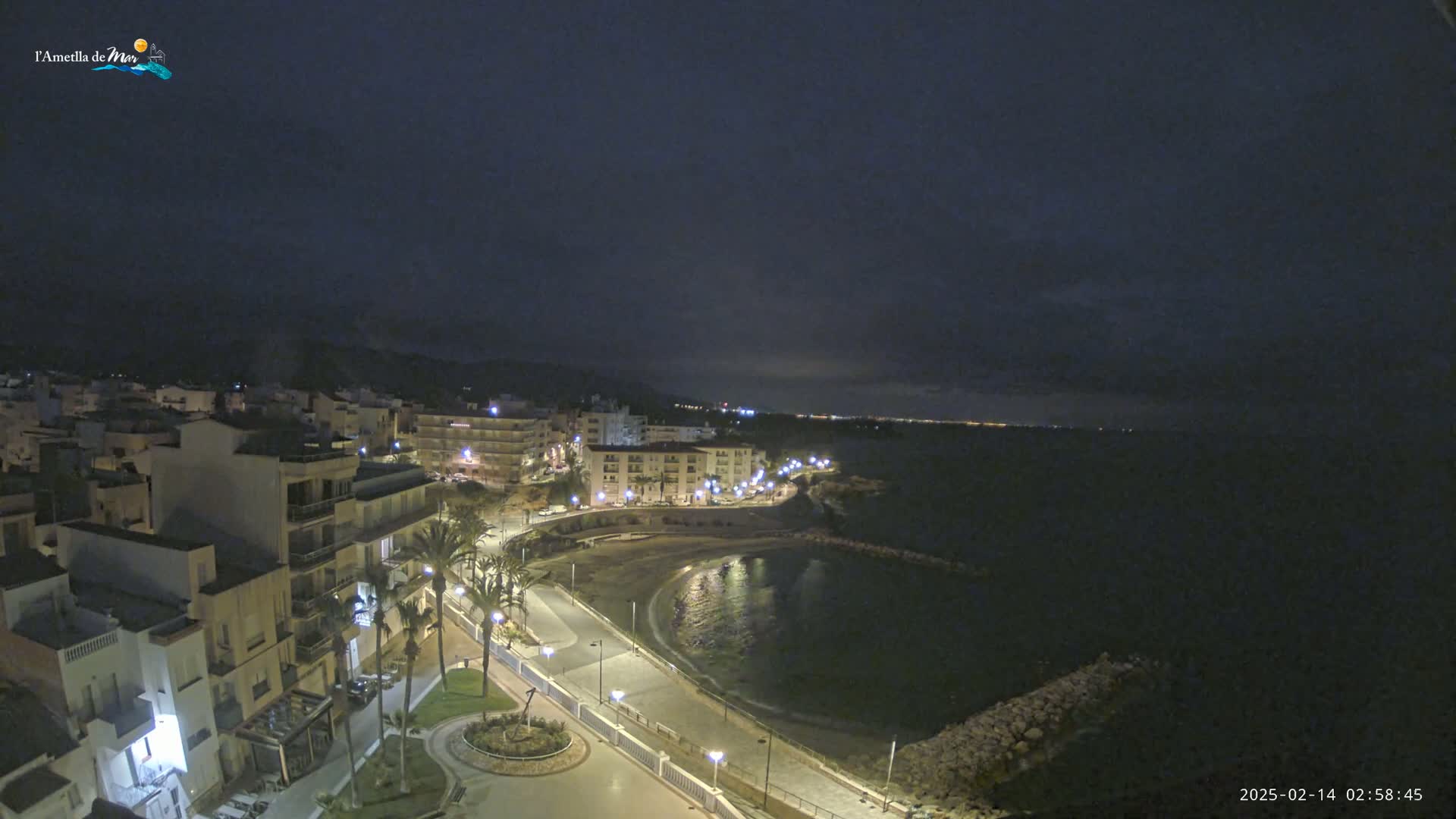A nighttime aerial view of a coastal town with a crescent-shaped bay, under a dark, mostly cloudy sky.
