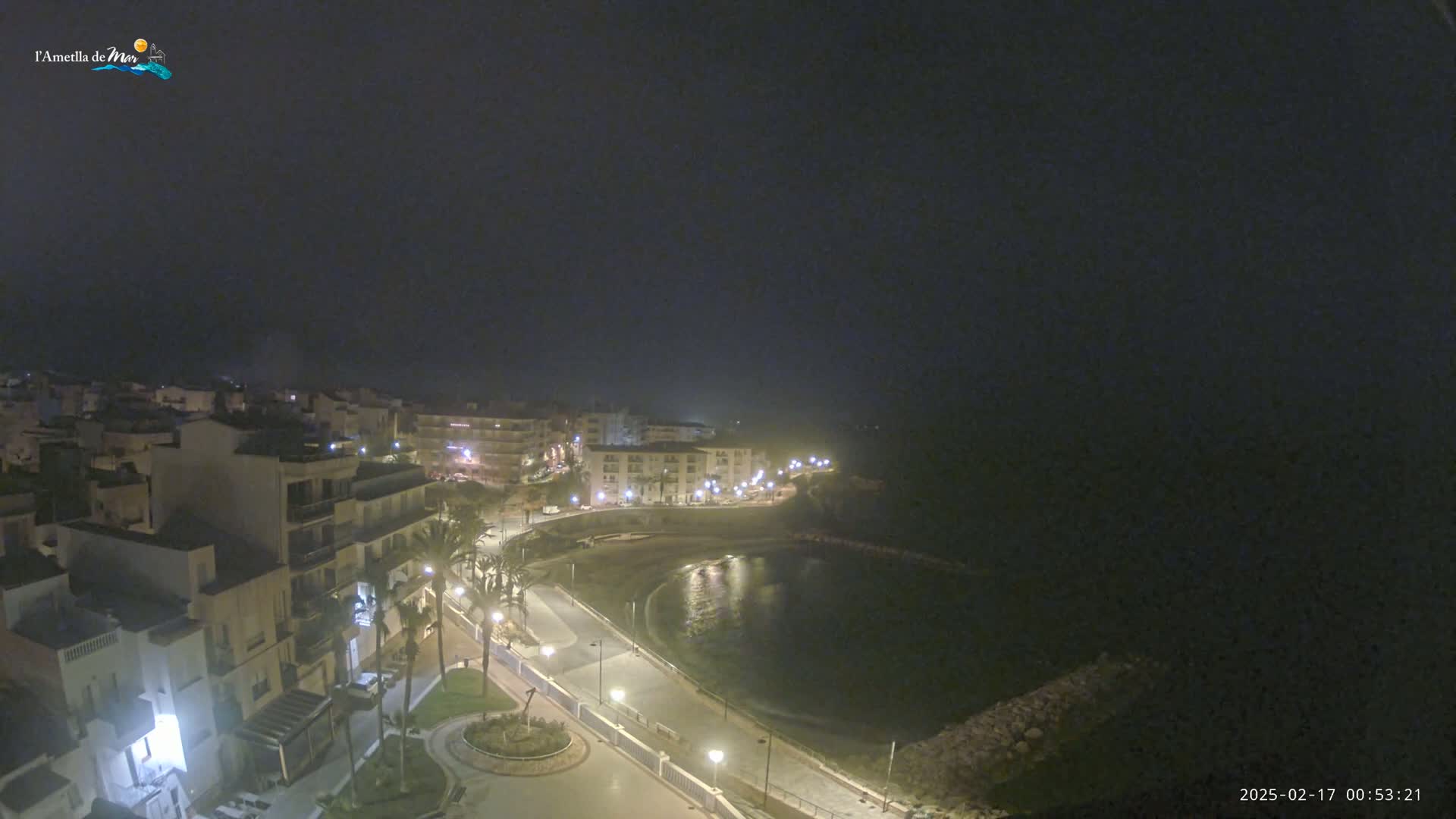 A nighttime, hazy view of a coastal town with illuminated buildings and a calm bay.