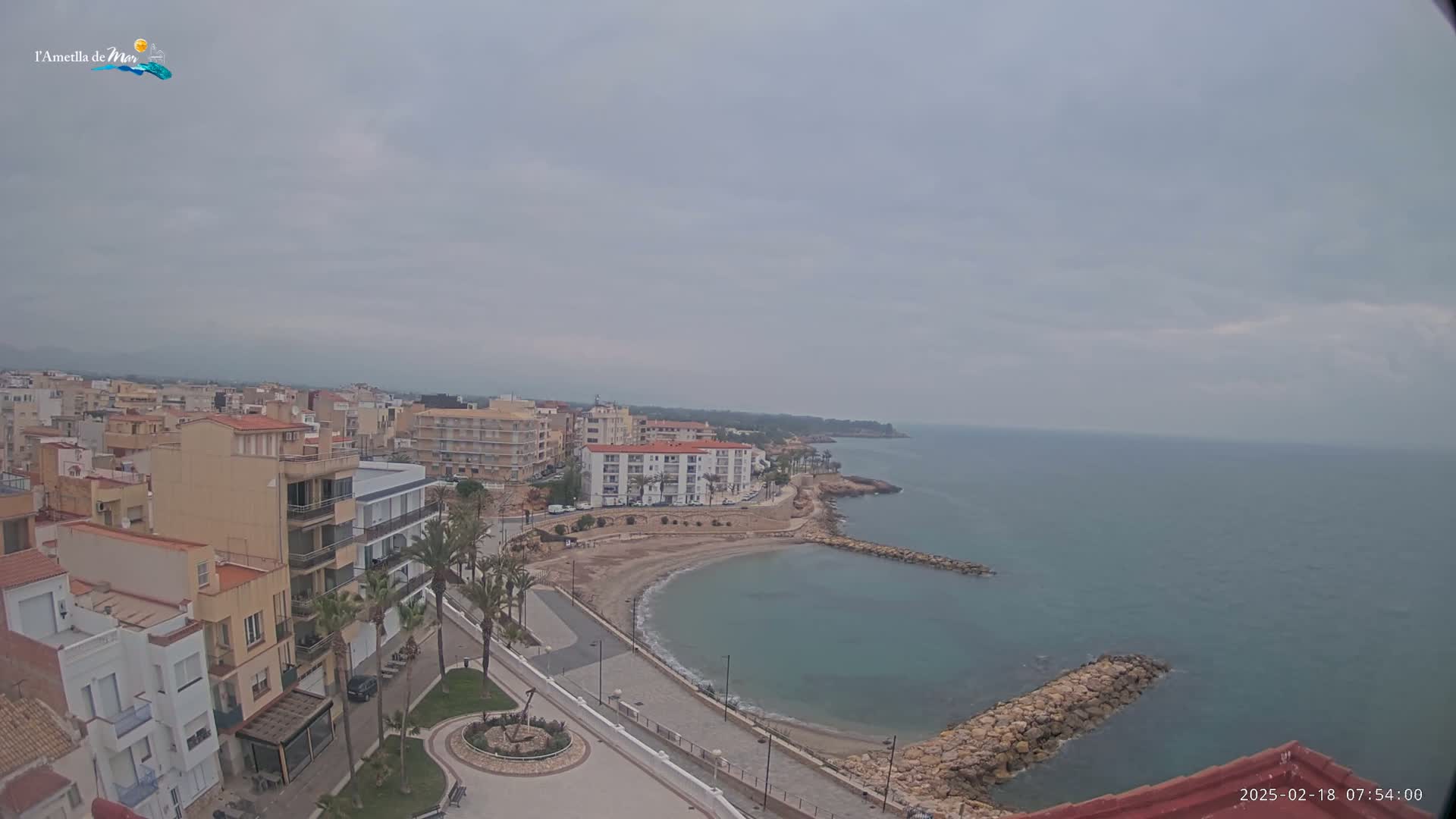 An elevated view shows a coastal town on an overcast day, with buildings lining a small, calm bay that meets a larger body of sea.