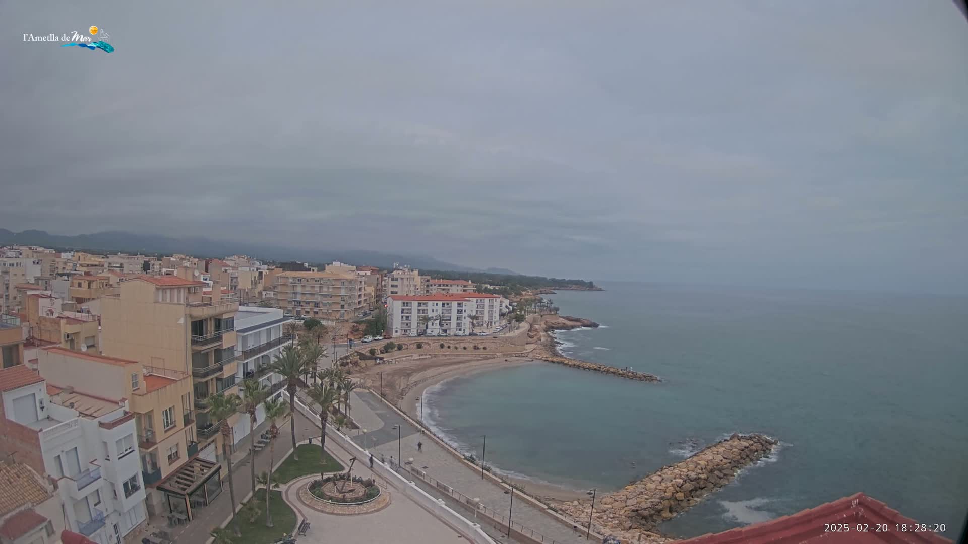 A coastal town with buildings, a small sandy cove, and a calm sea under an overcast sky.