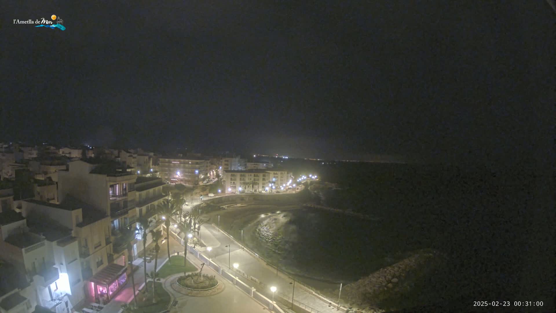 A nighttime, high-angle view of a coastal town with buildings illuminated along a dark, calm bay.