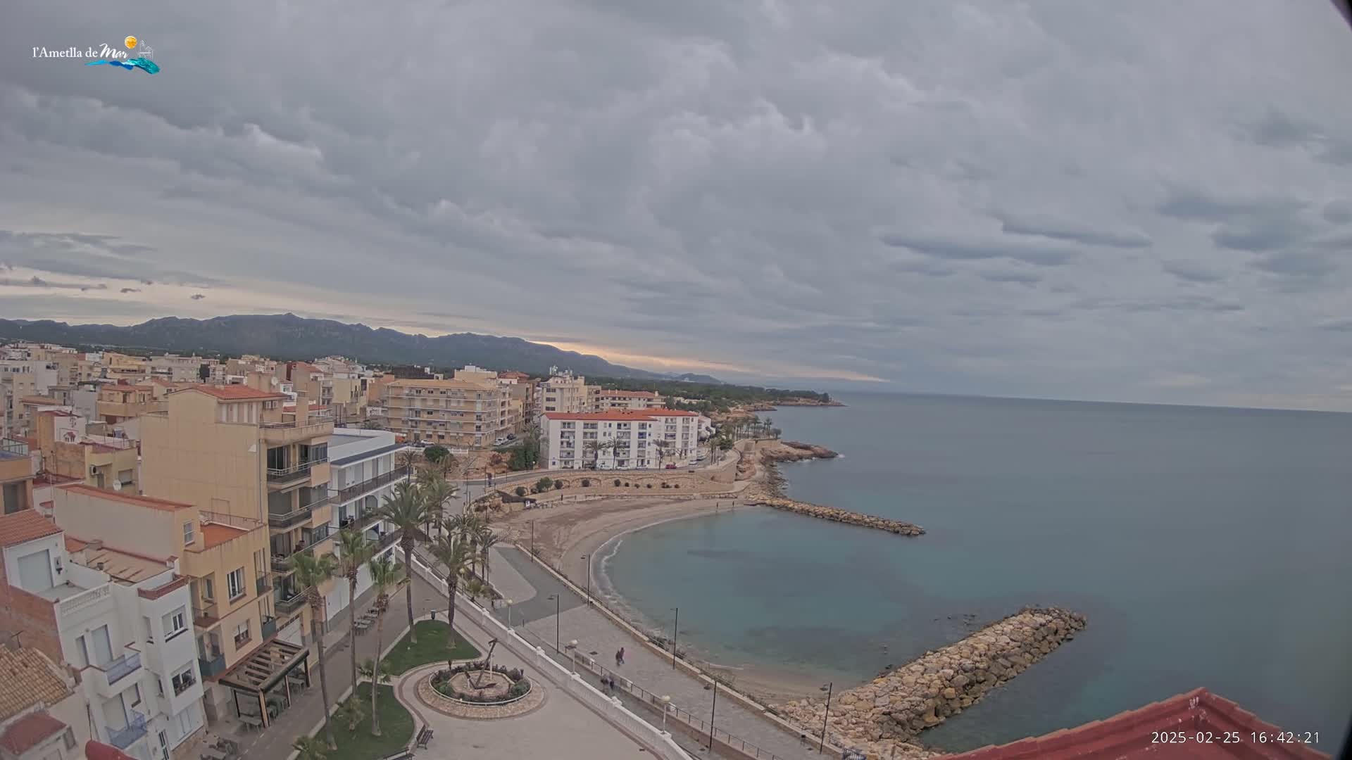 A coastal town with buildings and a small sandy cove is seen under a cloudy sky.