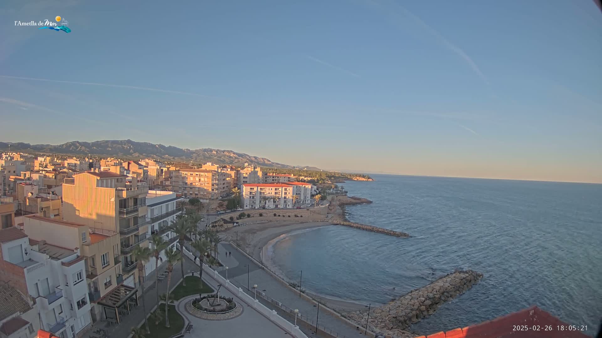 A coastal town with buildings, a small beach, and calm ocean under a clear, bright sky.