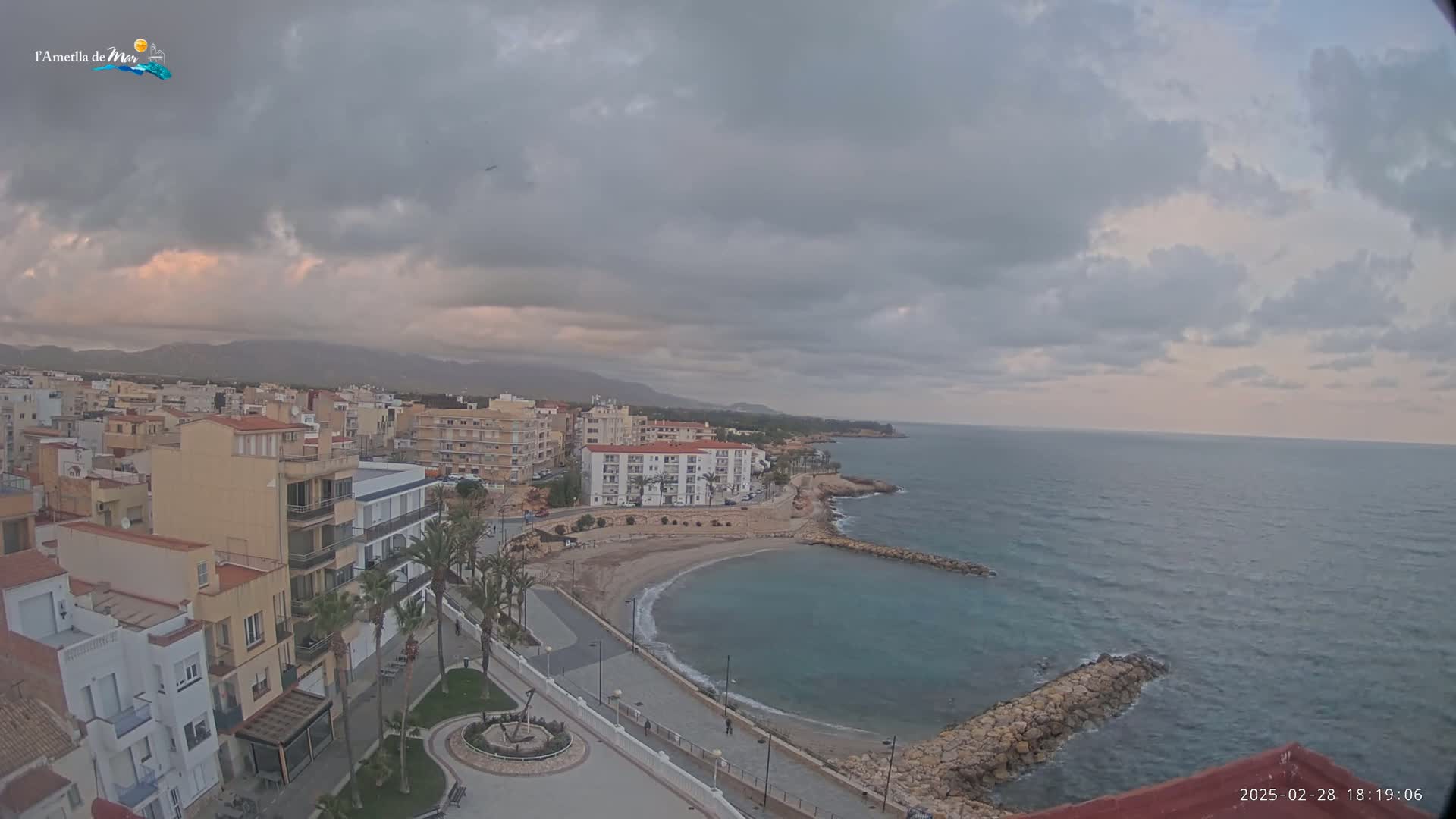 An overcast sky hangs over a coastal town with a small, sandy cove and calm ocean waters.