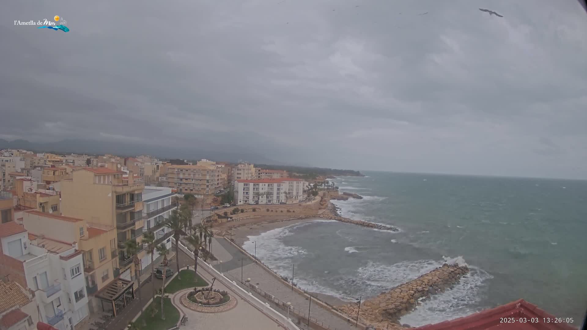 A coastal town under an overcast sky, with a somewhat choppy sea and birds flying overhead.