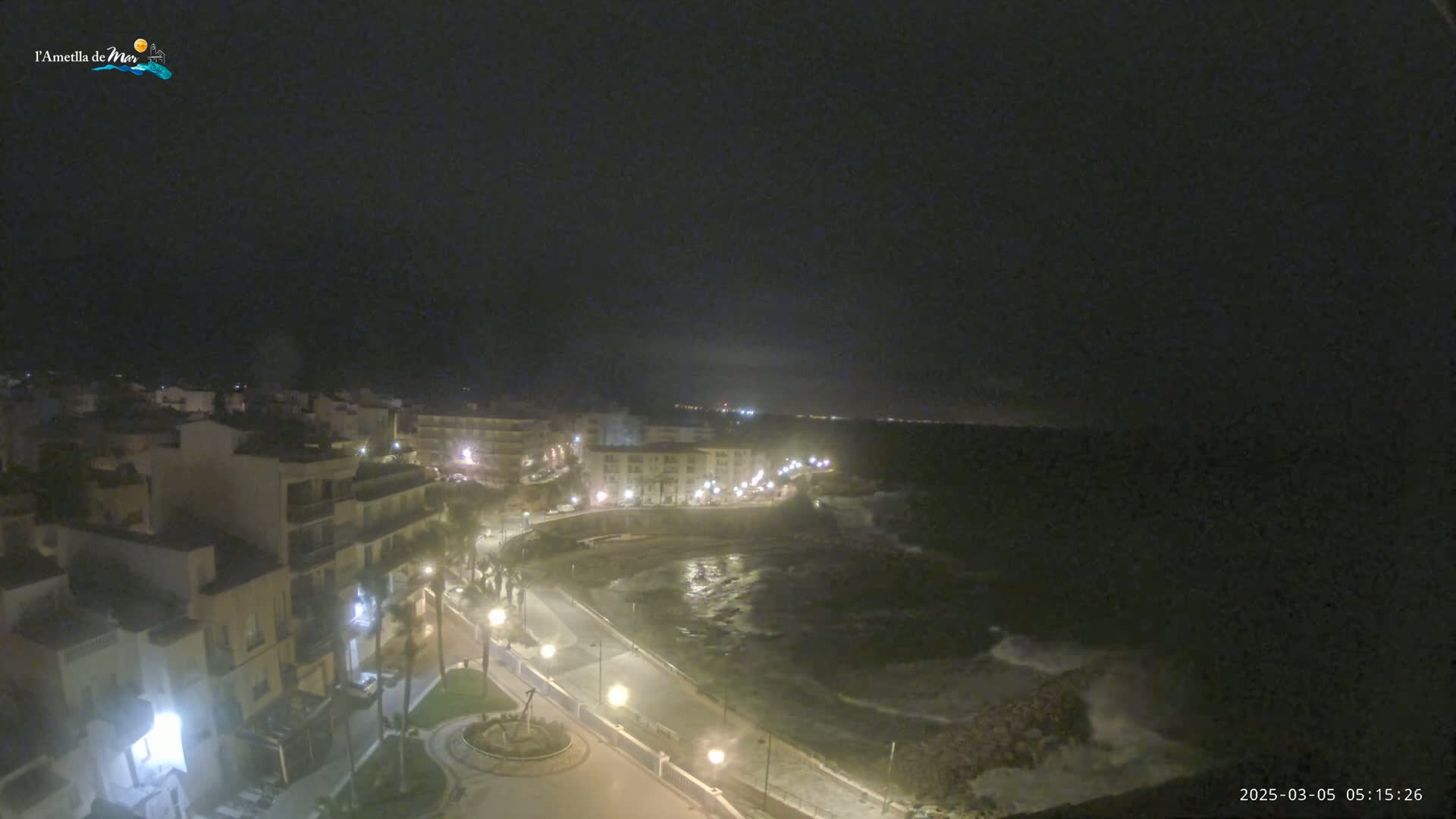 A nighttime, aerial view of a coastal town with a dark, wavy ocean and buildings illuminated by streetlights.