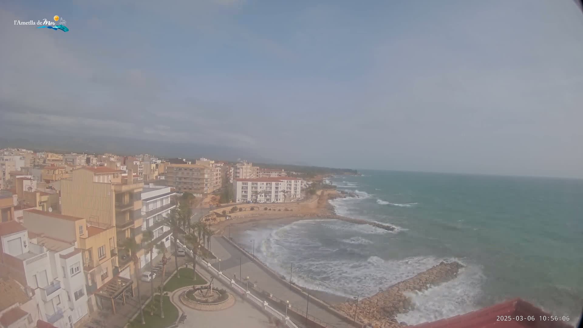 A coastal town with buildings and a beachfront road overlooks a somewhat choppy sea under a hazy sky.