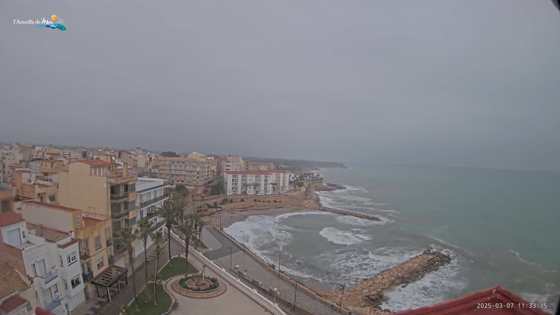 A coastal town on a cloudy day with choppy waves crashing against a rocky shoreline.