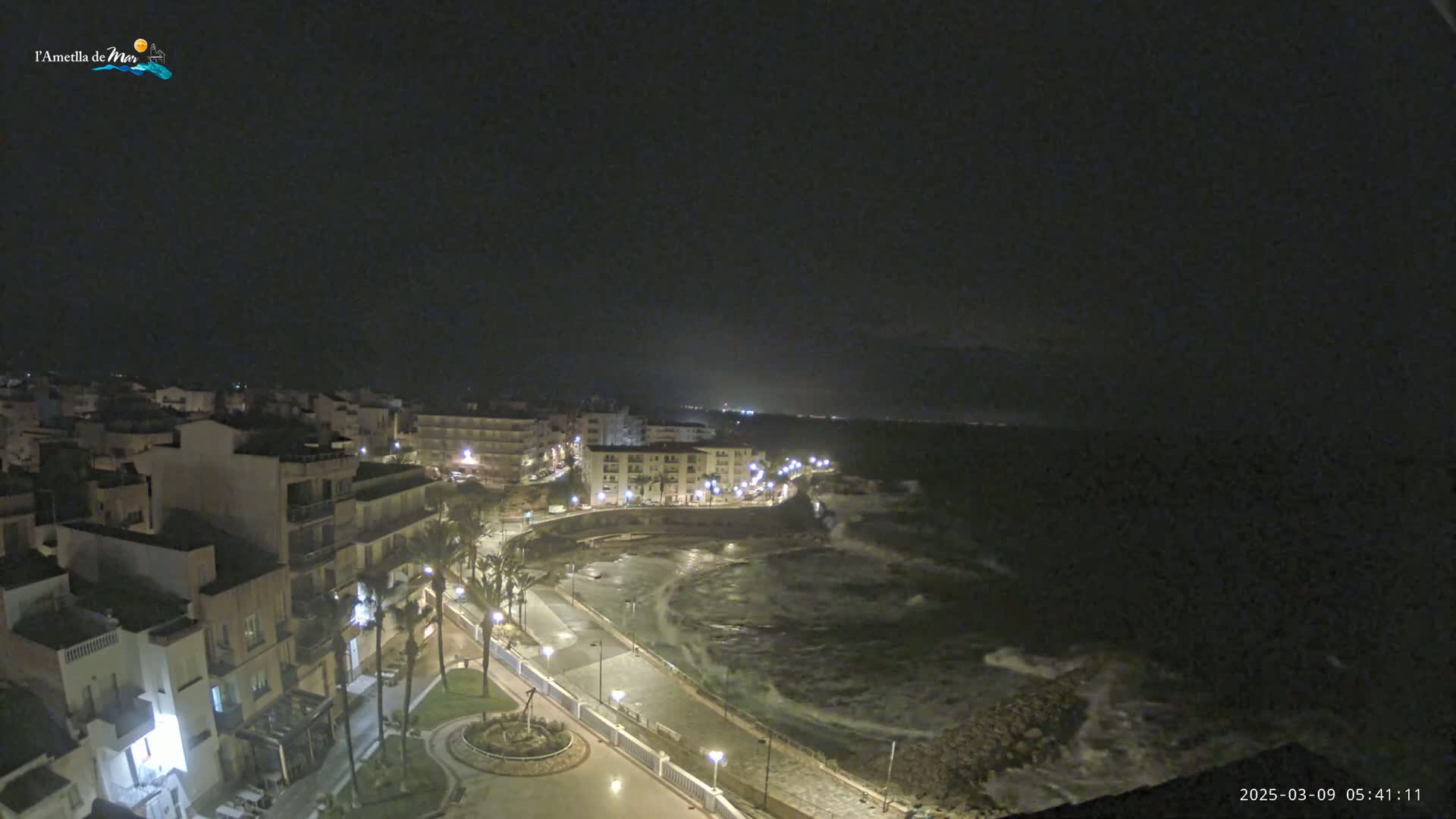 A nighttime coastal town with a rocky shoreline and choppy waves under a dark sky.