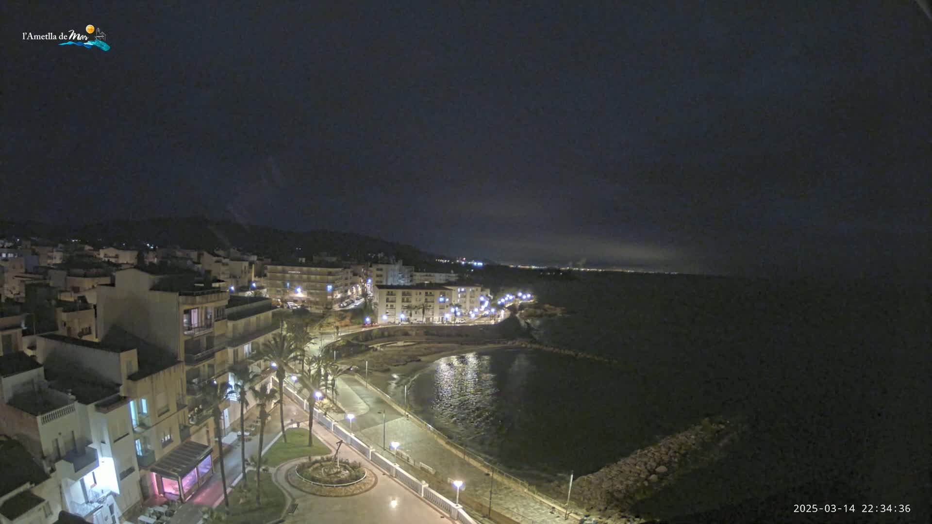 A nighttime view of a coastal town with a calm sea under a dark sky.