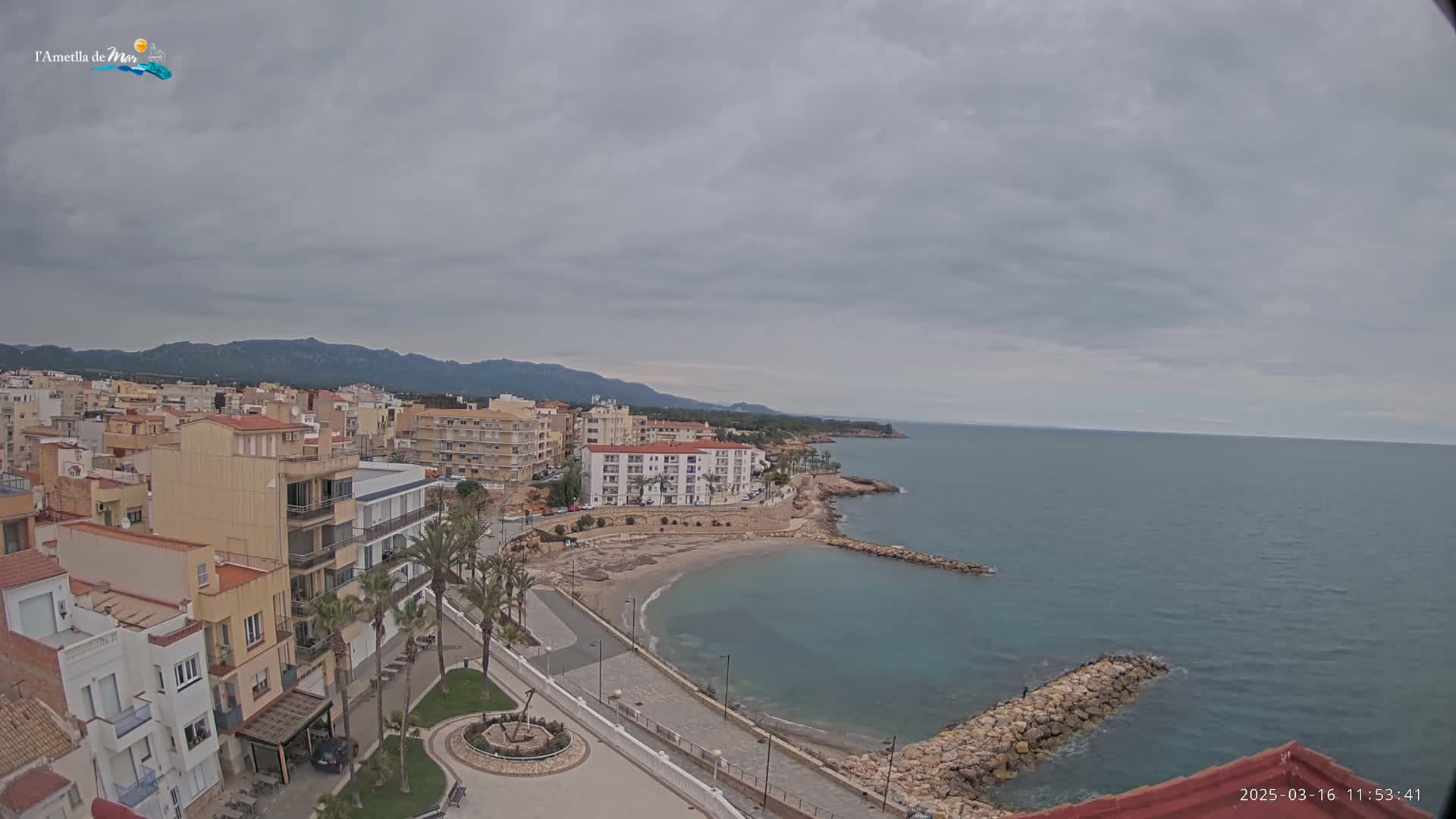 An elevated view shows a coastal town under an overcast sky, with a small, sandy cove and calm sea.