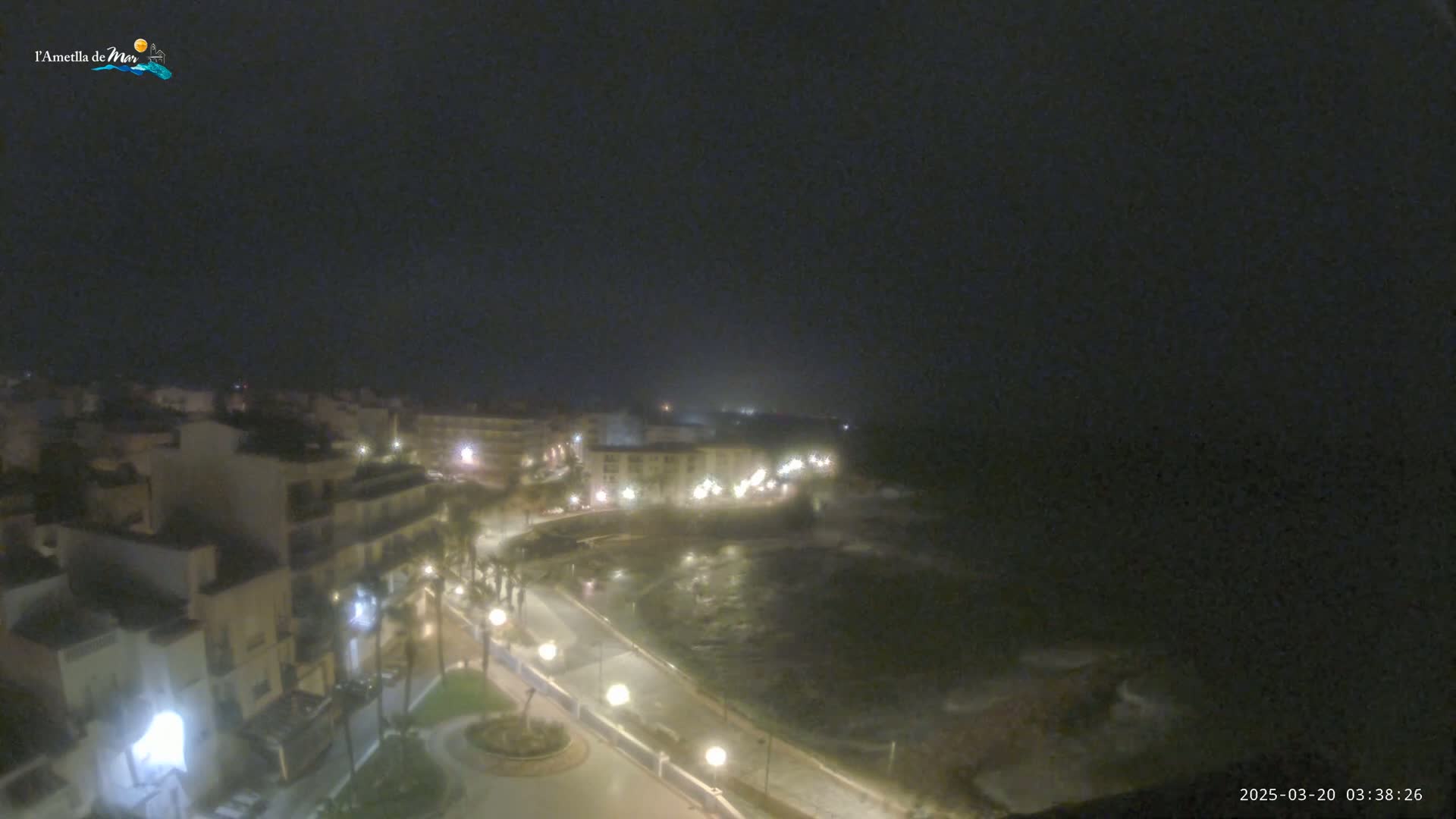 A nighttime, hazy view of a coastal town with a dark ocean, illuminated streets, and buildings.
