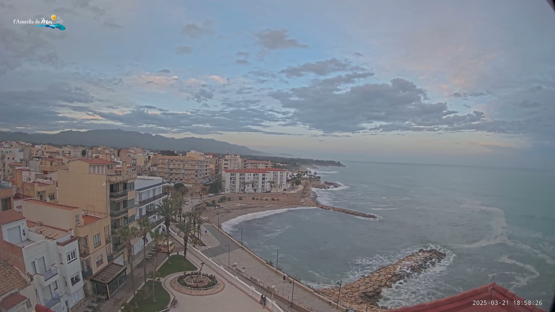An elevated view shows a coastal town under a partly cloudy sky, with a rocky shoreline and somewhat choppy ocean.