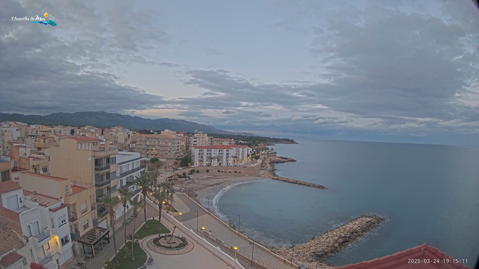 An overcast sky overlooks a coastal town with buildings, palm trees, a small beach, and a calm sea.
