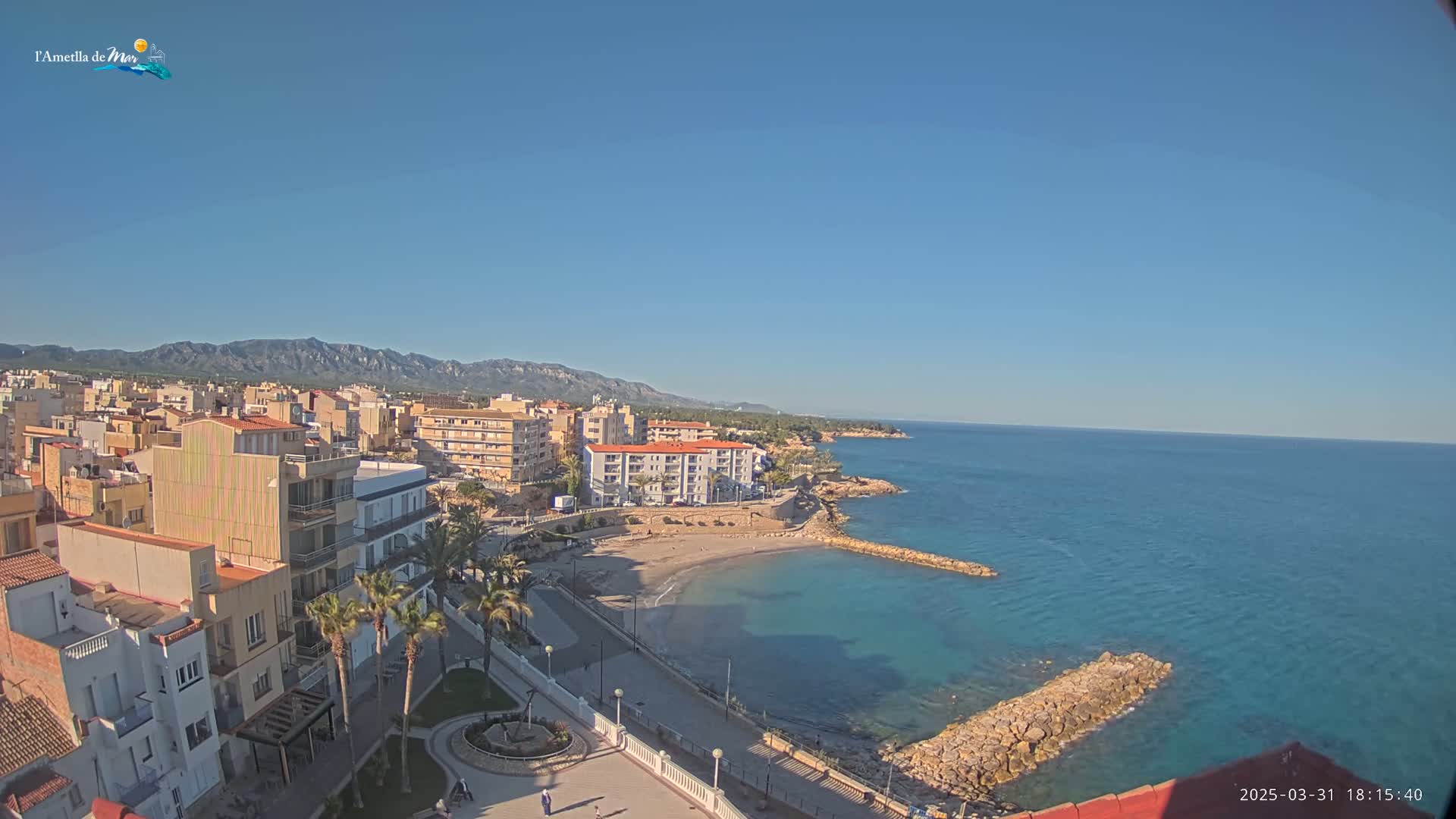 A coastal town with buildings, a small beach, and a clear blue ocean under a sunny sky is visible from an elevated viewpoint.