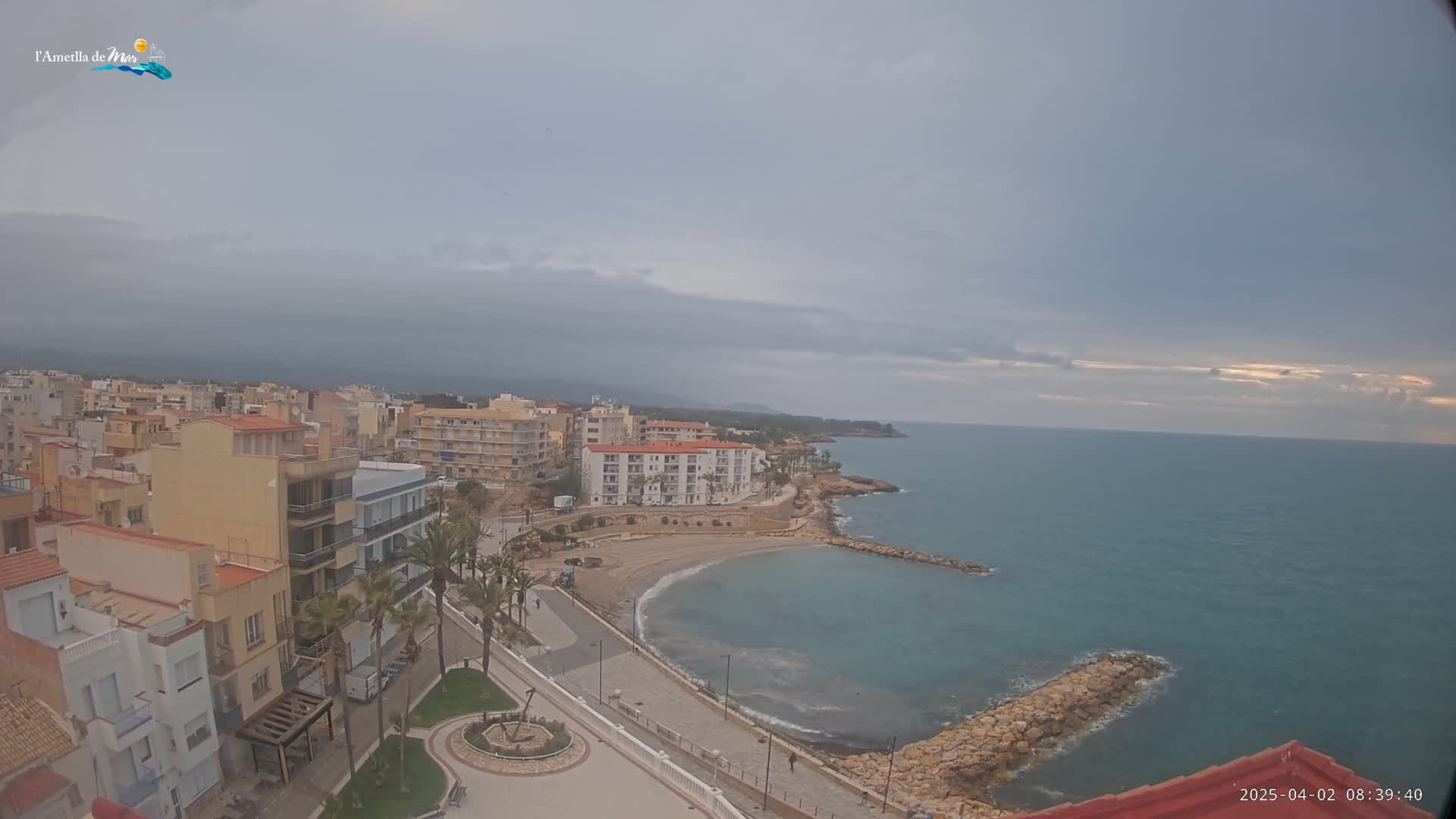 An overcast sky hangs over a coastal town with buildings, a small beach, and a calm sea.