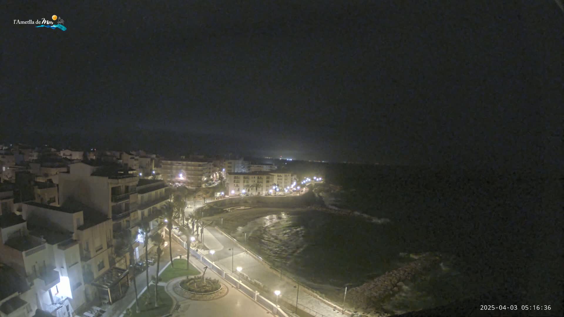 A nighttime view of a coastal town with a dark sky and gently waving water.
