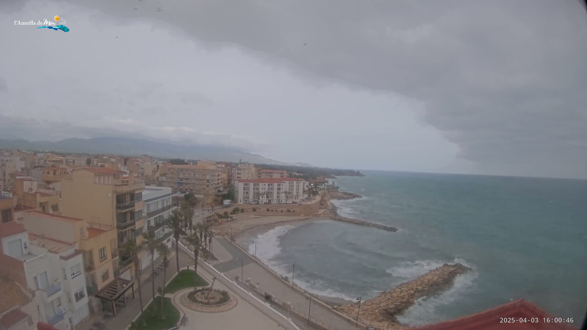 An overcast coastal town with a small beach and choppy sea is viewed from above.