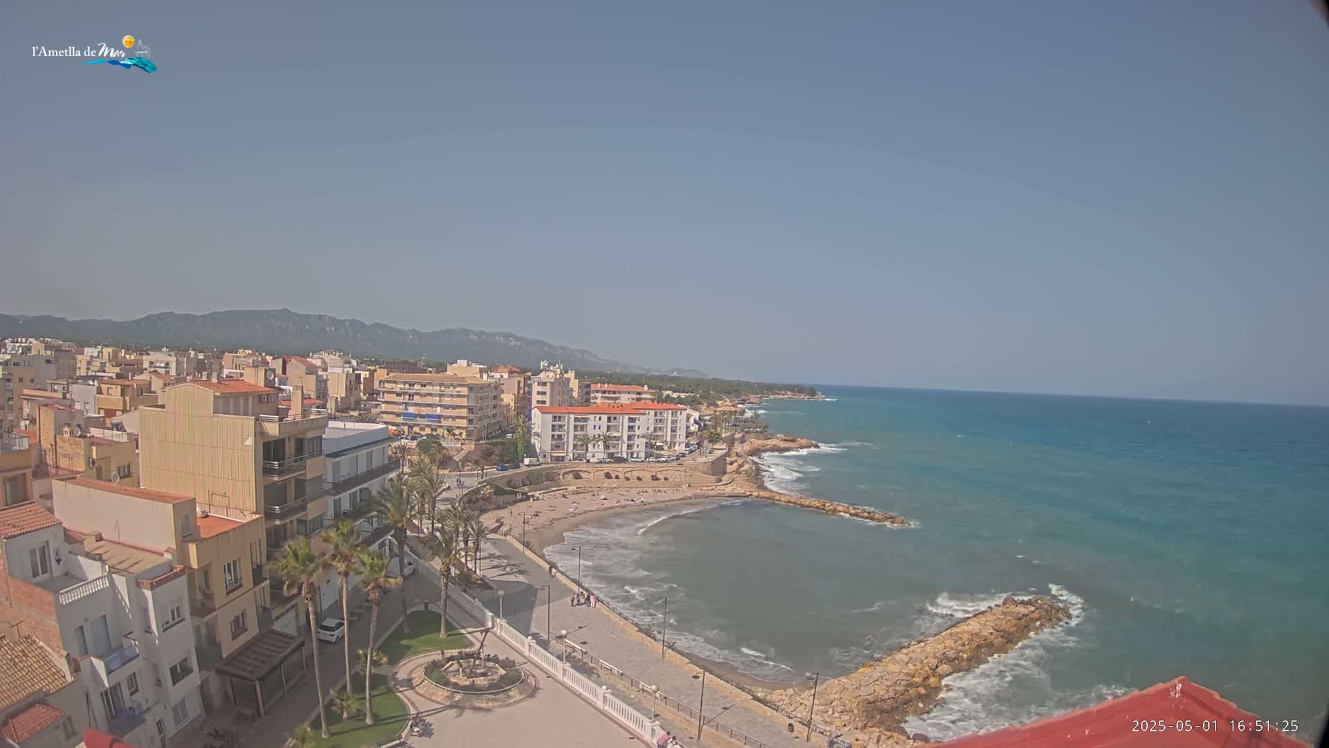 A coastal town with buildings, a beach, and calm blue ocean under a clear sky.