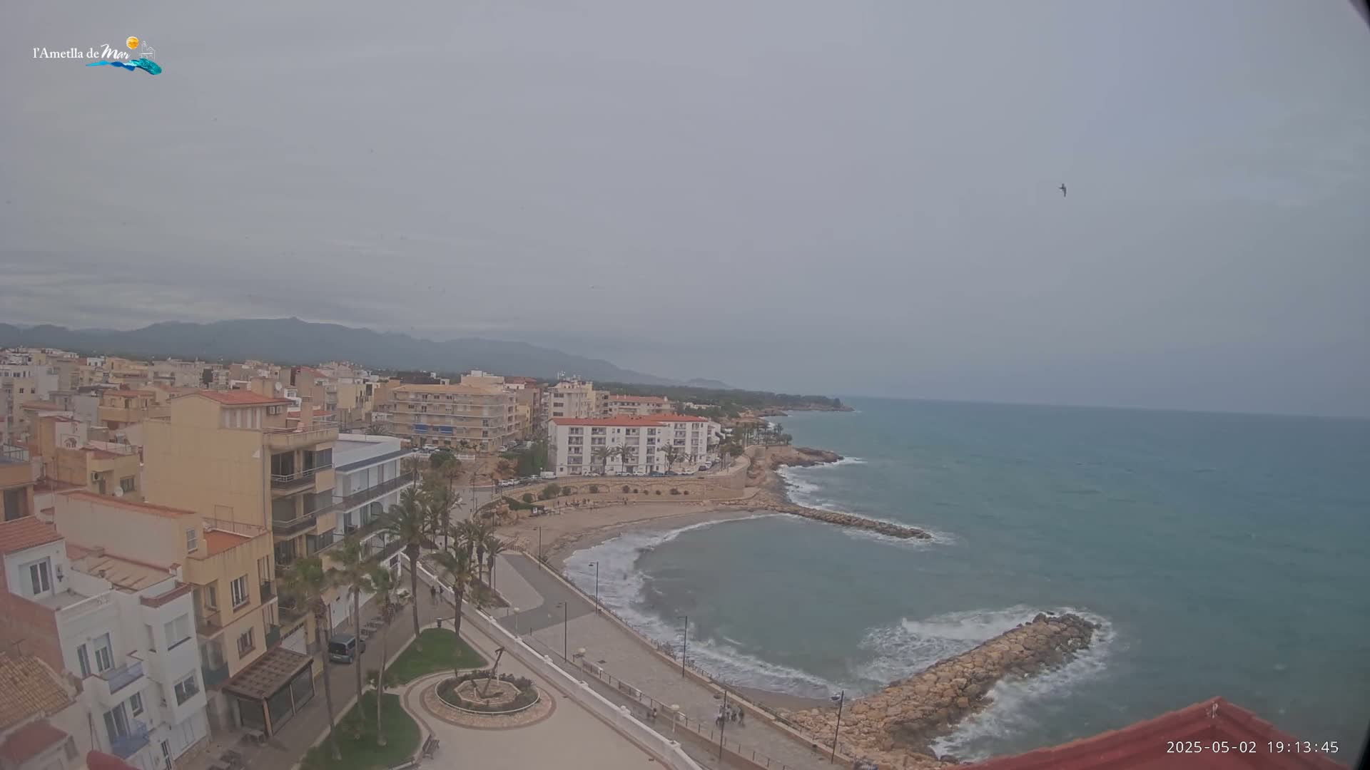 A coastal town under an overcast sky, with a small beach and calm waves lapping against a rocky shore.