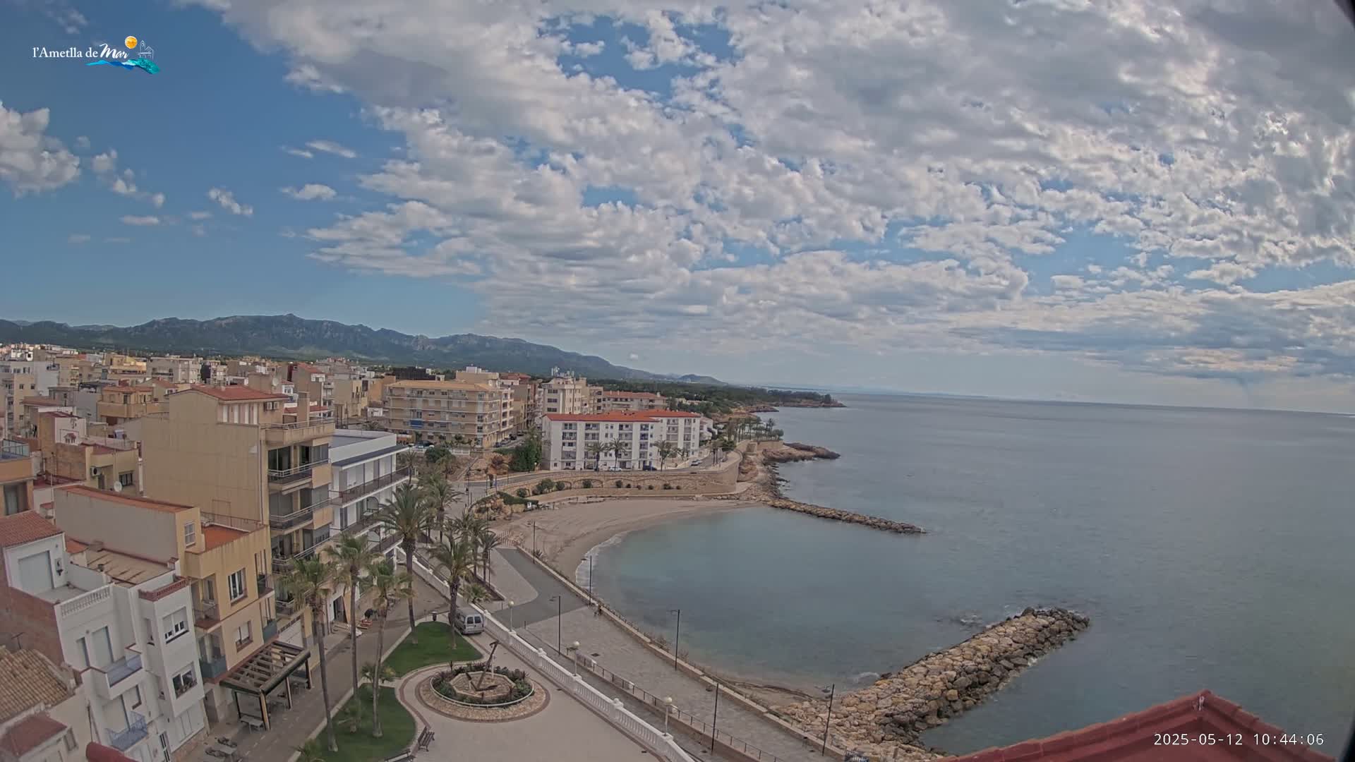 A partly cloudy day overlooks a coastal town with a small, calm bay and mountains in the distance.