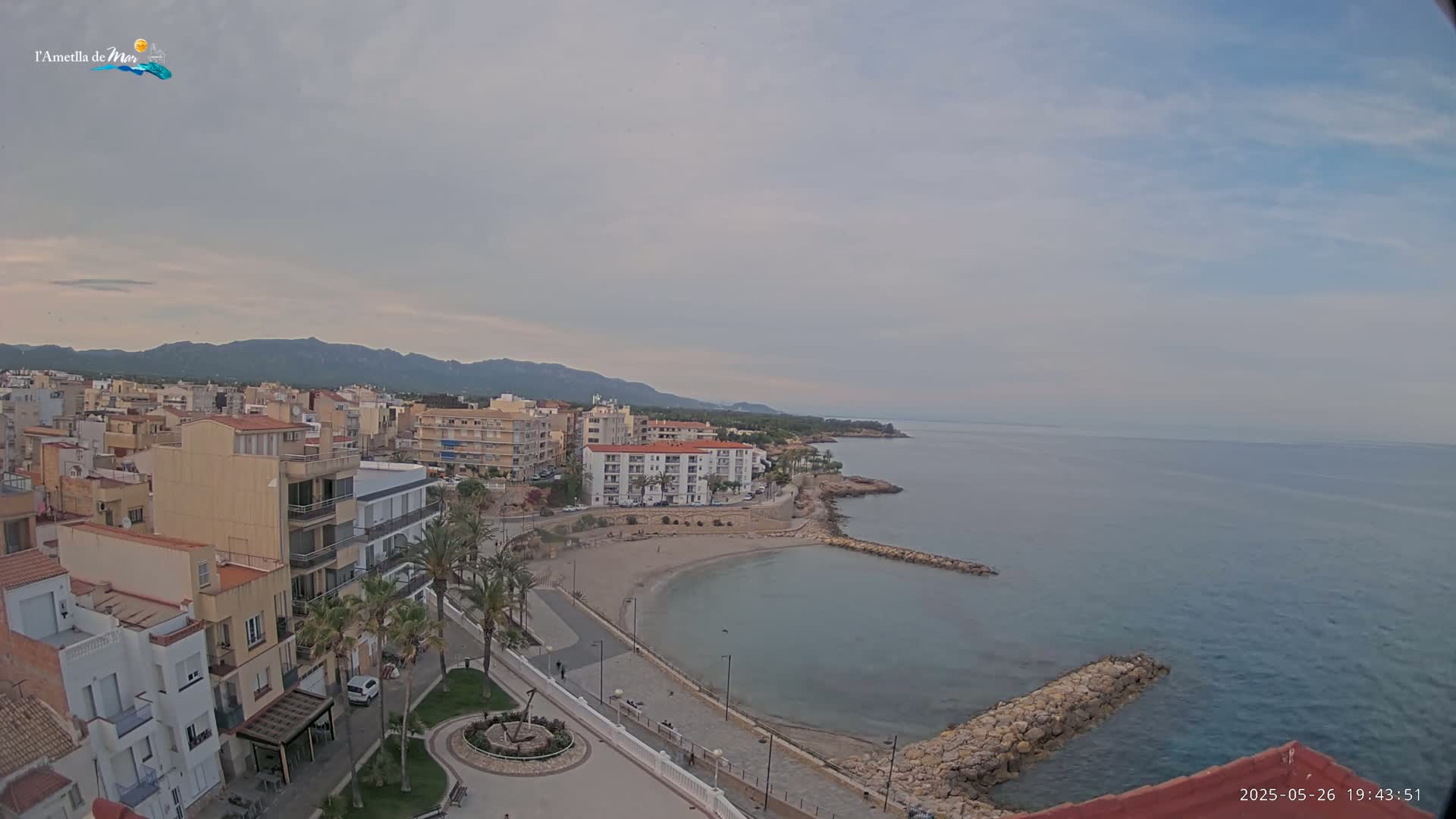An overcast day reveals a coastal town with a small sandy beach, calm water, and distant mountains.