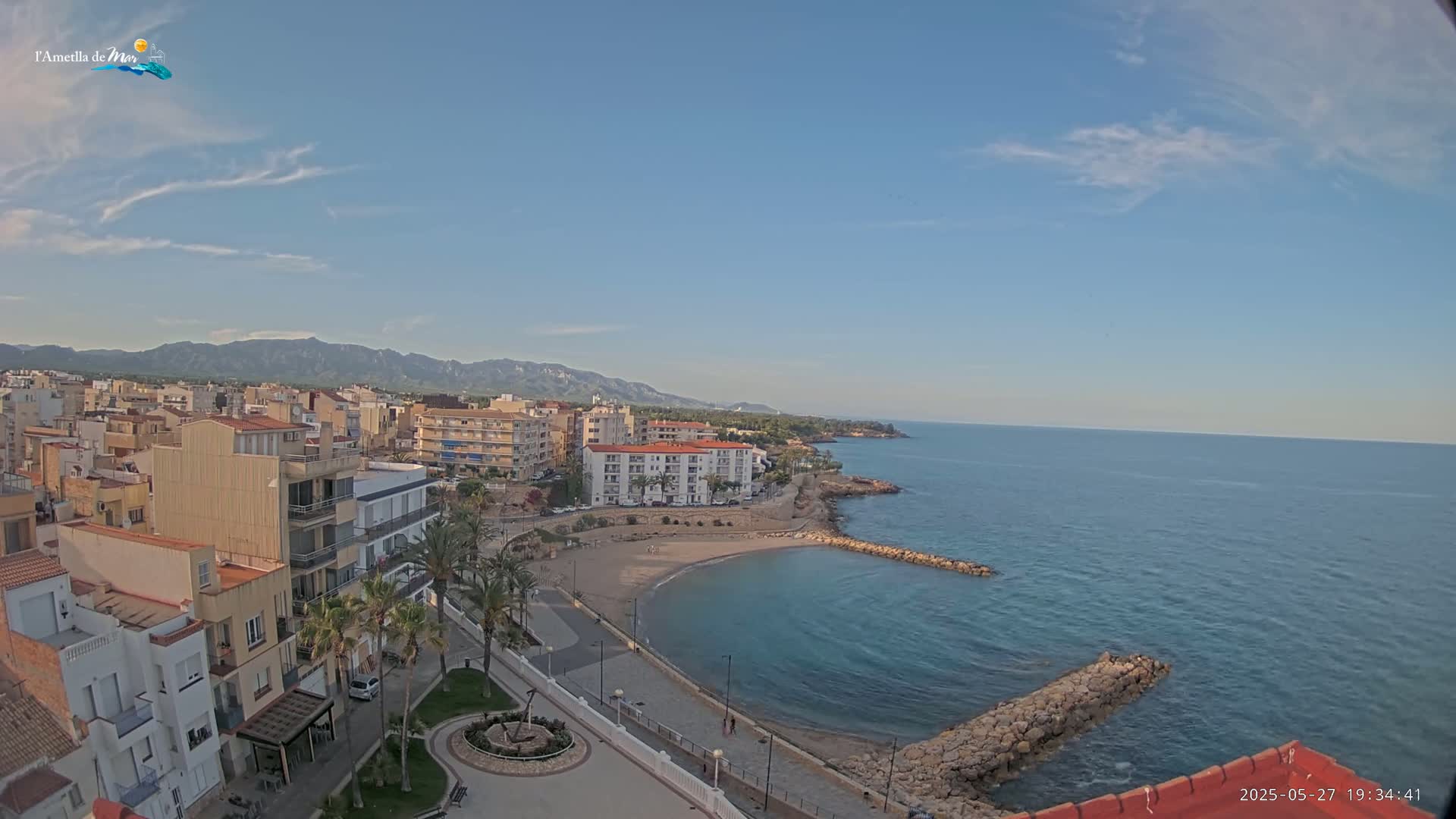 A coastal town with buildings, a small beach, and calm ocean under a mostly clear sky.
