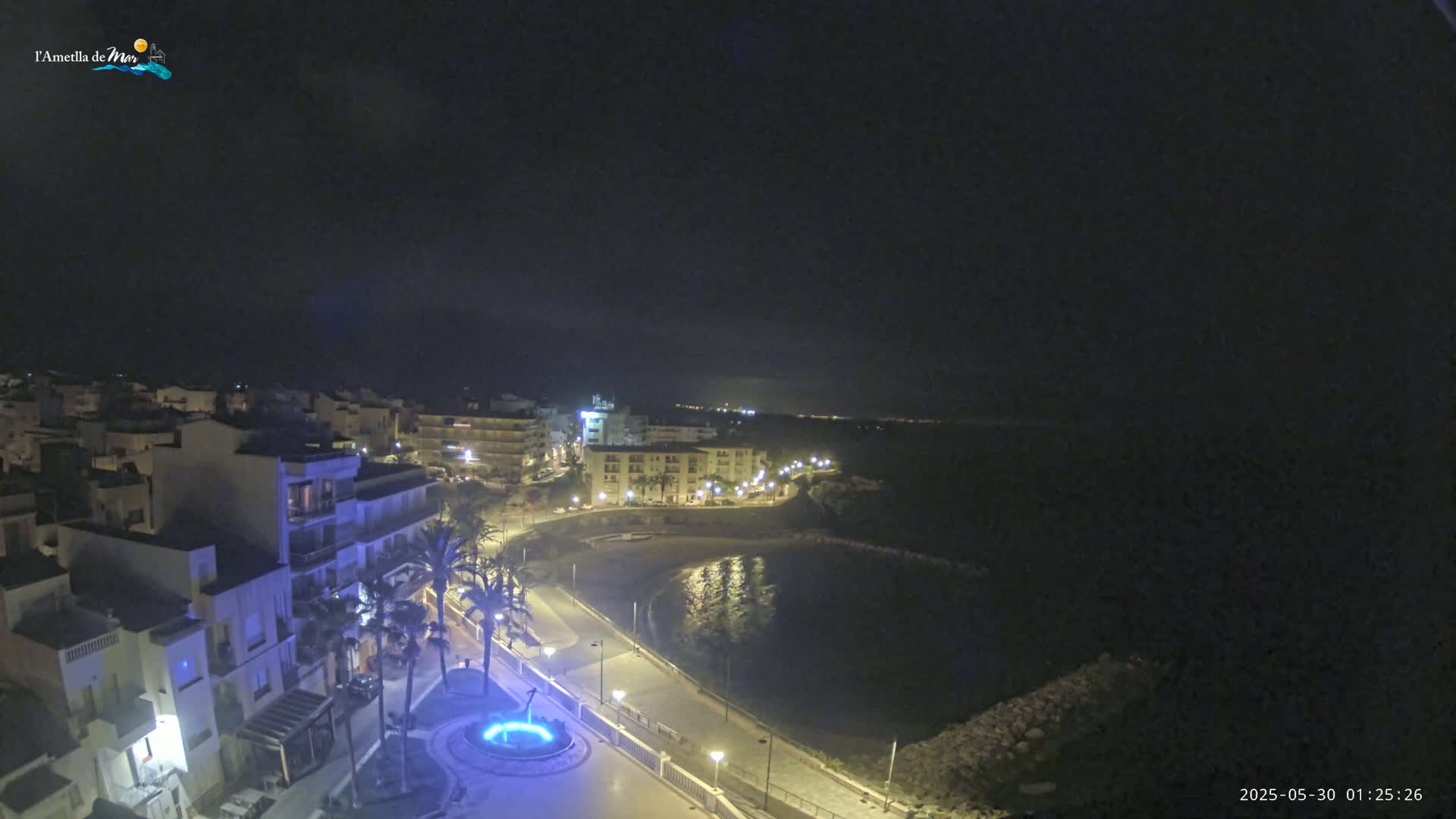 A nighttime view of a coastal town with a calm bay, illuminated by streetlights.