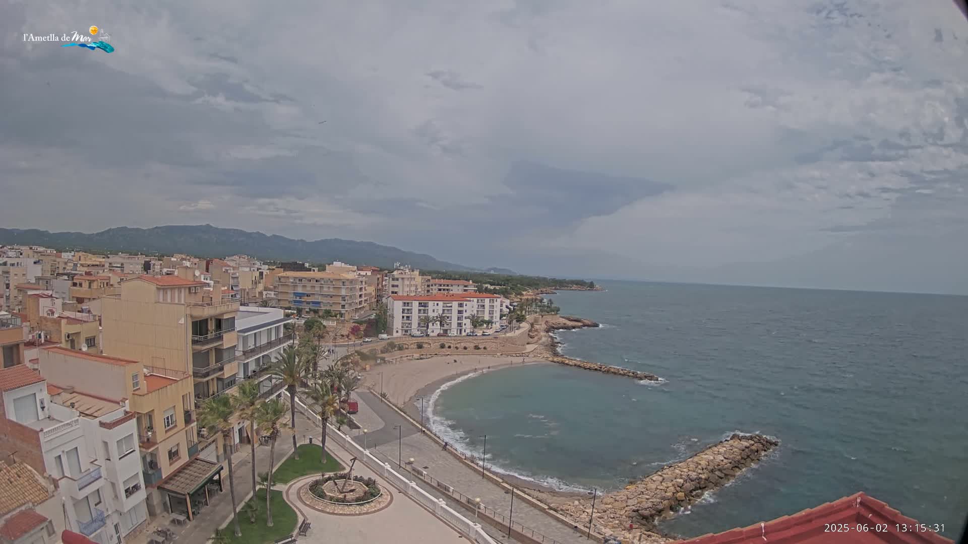 A coastal town with buildings, a small beach, and a calm sea under a mostly cloudy sky.
