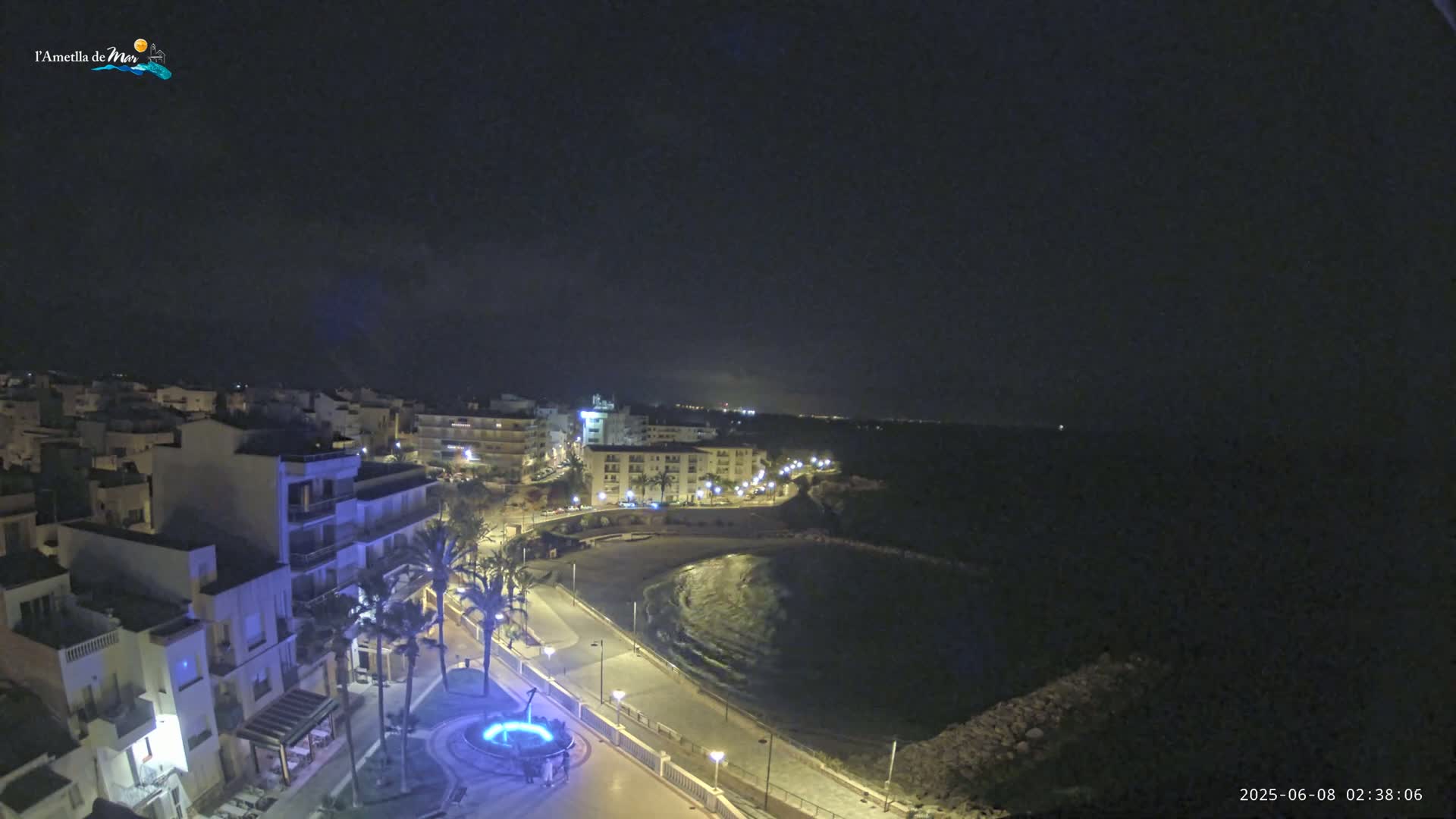 A nighttime aerial view of a coastal town with a calm bay, illuminated by streetlights.