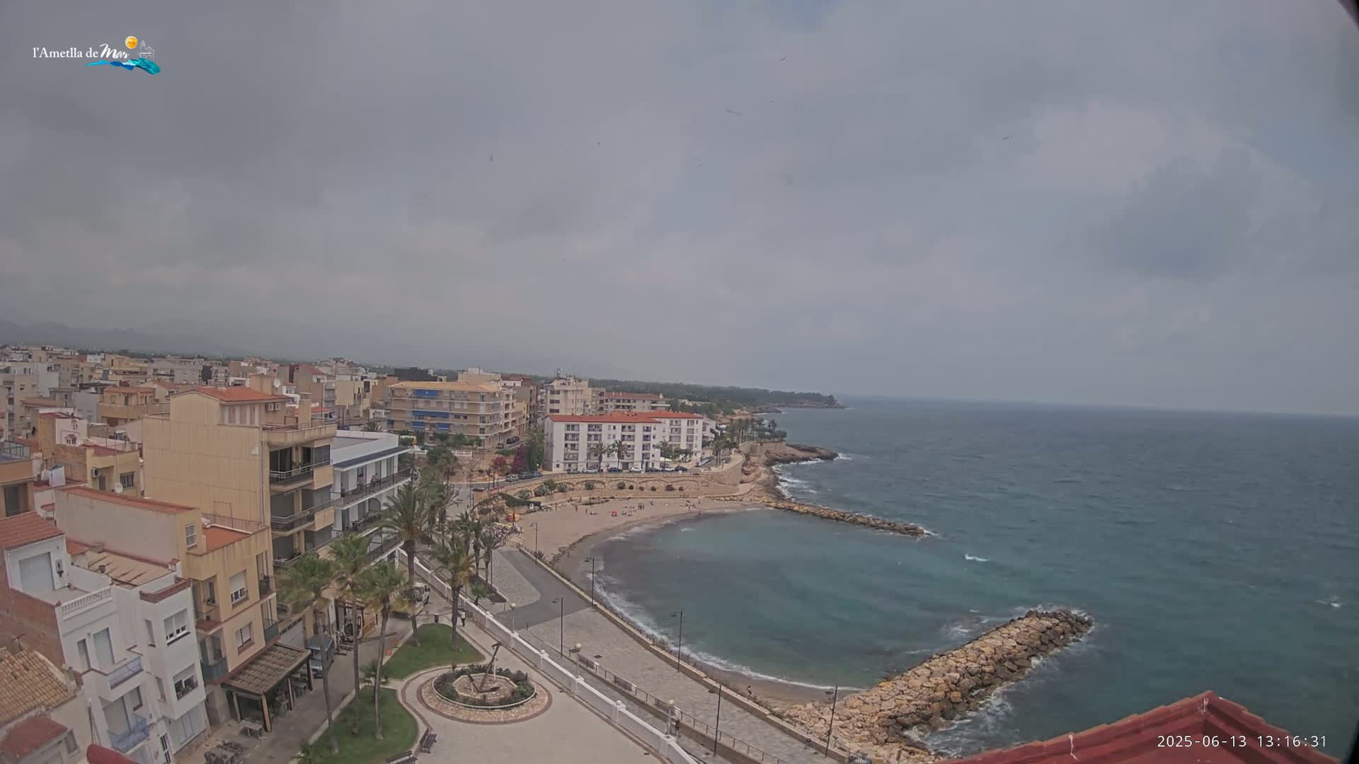 An overcast day reveals a coastal town with a small, sandy cove and calm ocean waters.