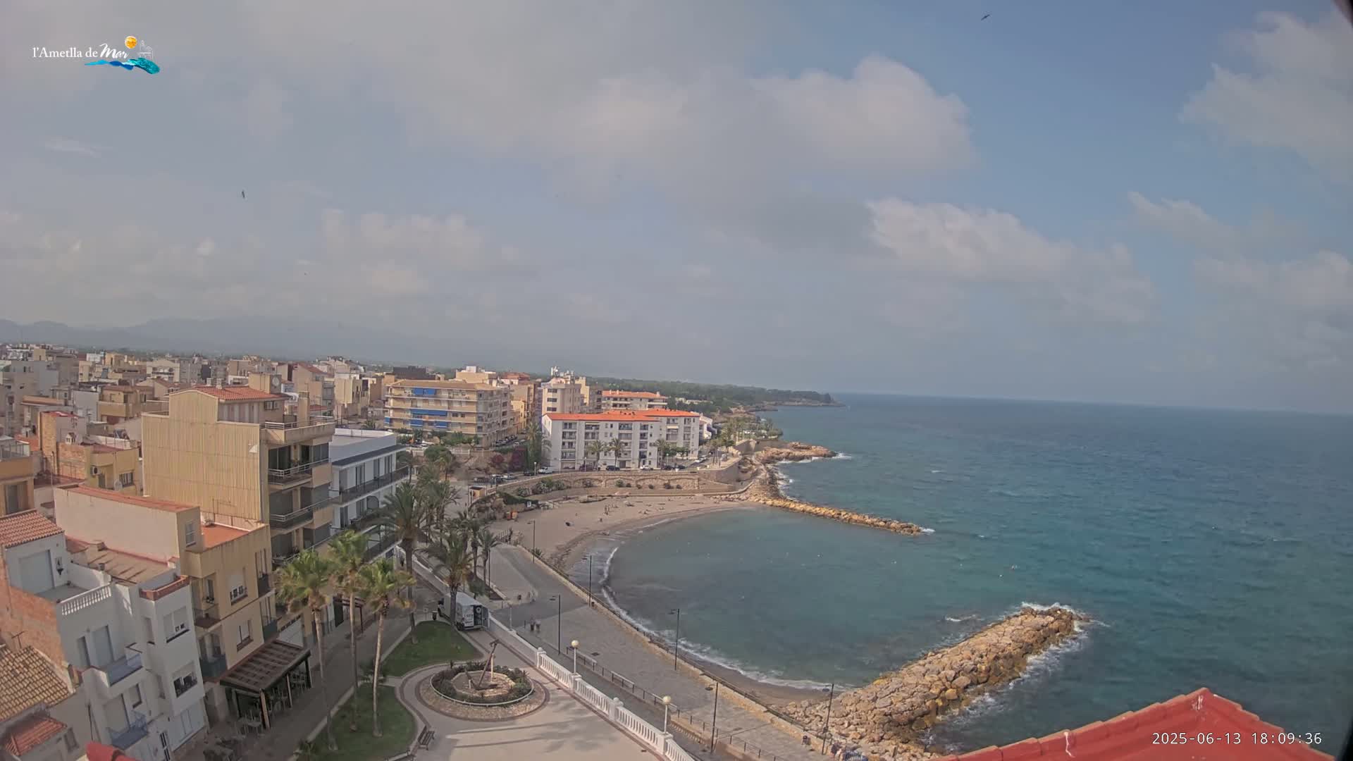 A partly cloudy day overlooks a coastal town with a small, sandy cove and calm ocean waters.