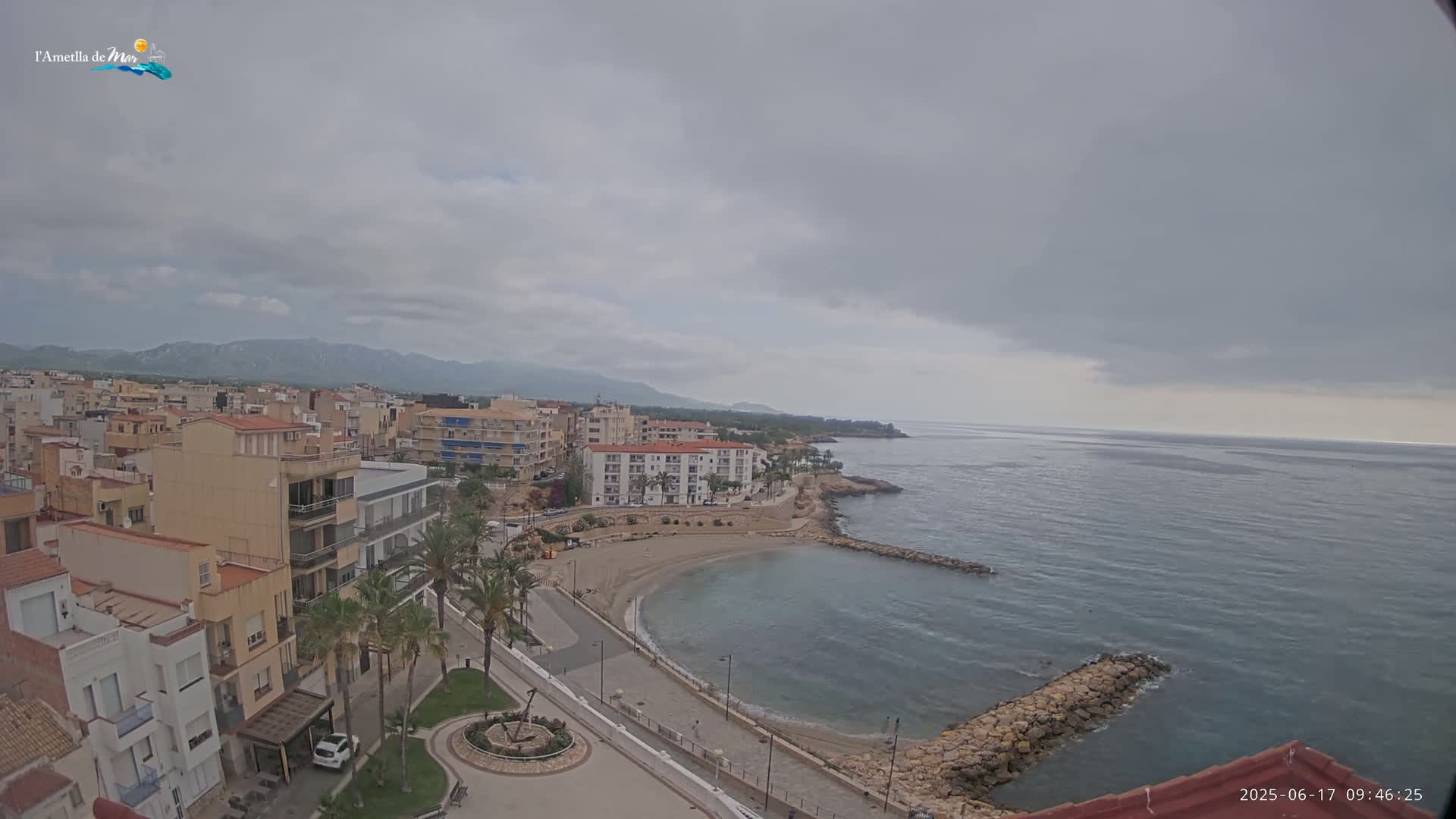 A coastal town with multi-story buildings sits beside a calm bay under an overcast sky.