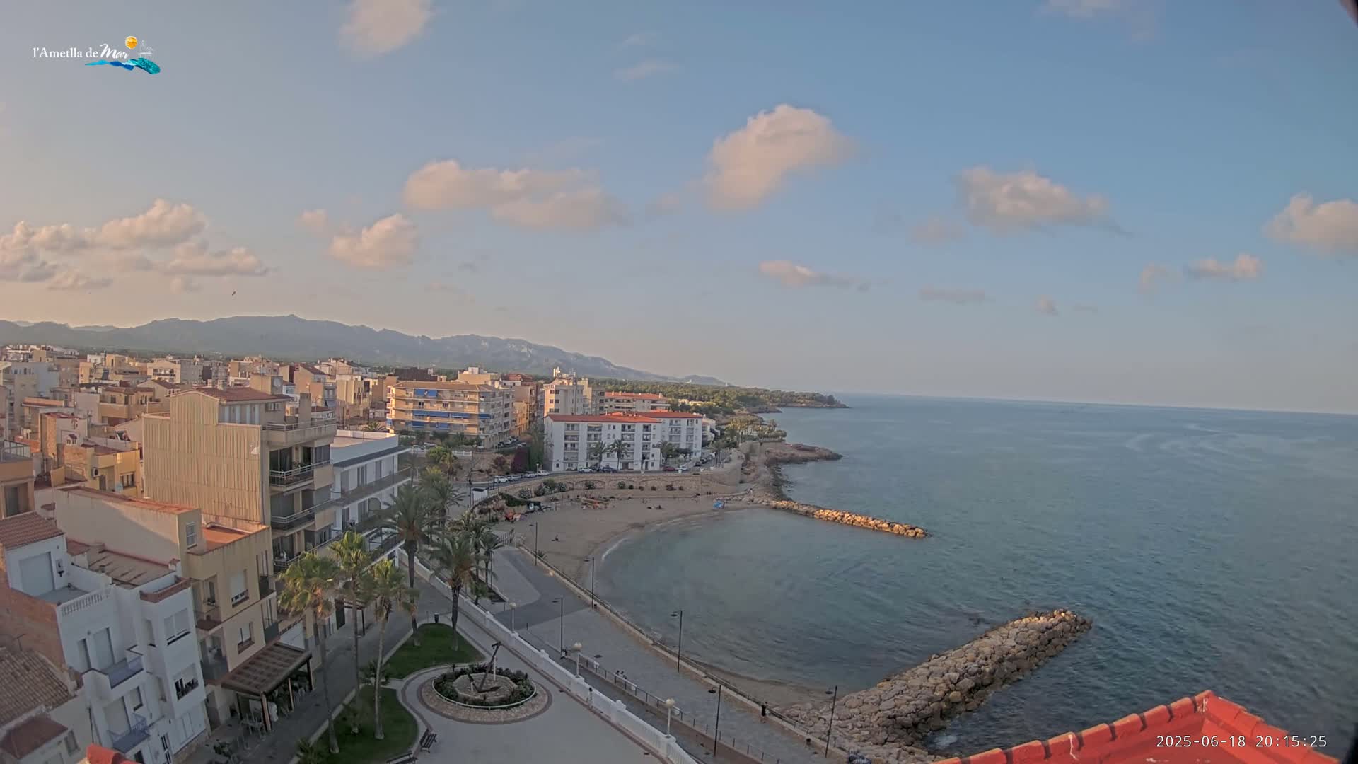A coastal town with buildings and palm trees overlooks a calm sea under a partly cloudy sky.