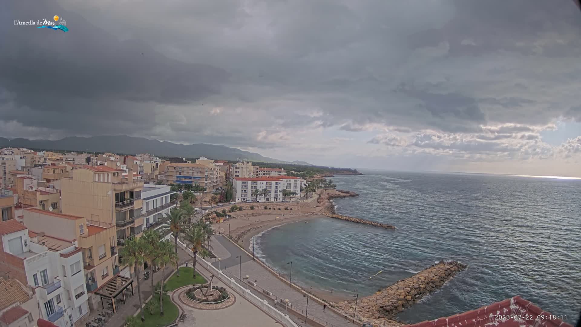 An overcast sky hangs over a coastal town with a small, crescent-shaped beach and calm ocean.