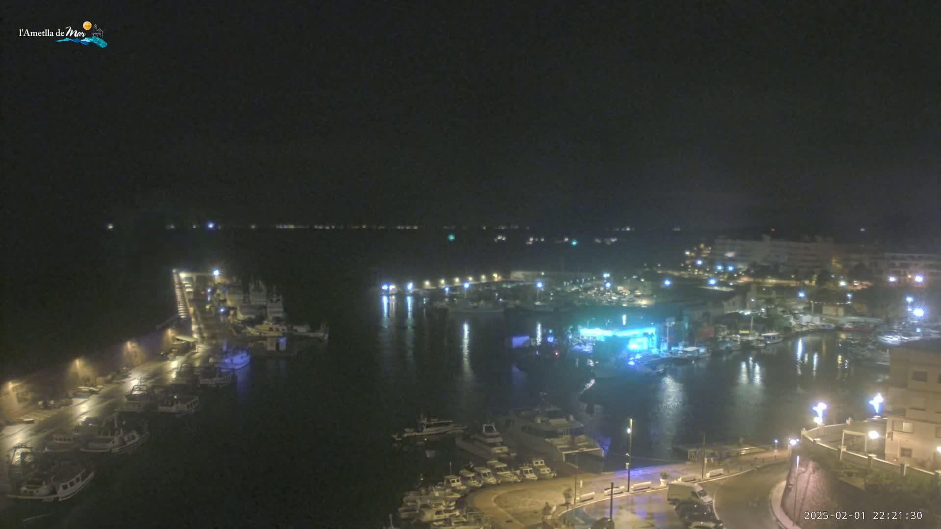 A nighttime aerial view of a harbor filled with boats, illuminated by lights reflecting on the water under a dark sky.