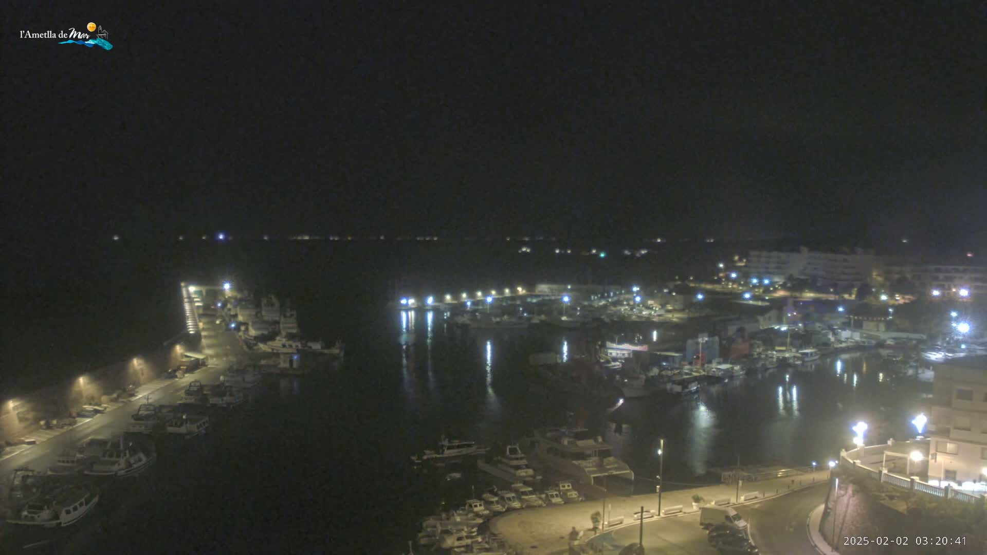 A nighttime, high-angle view of a harbor filled with boats, illuminated by lights along the waterfront and buildings.