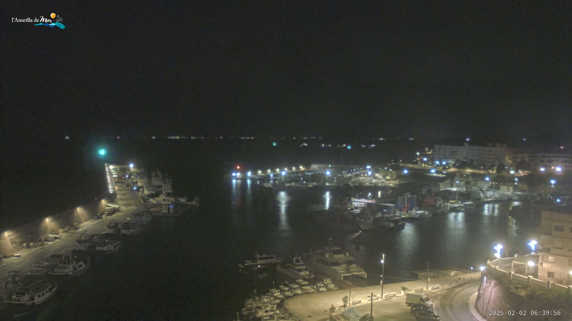 A nighttime view of a harbor filled with boats, illuminated by streetlights and building lights, under a dark, clear sky.