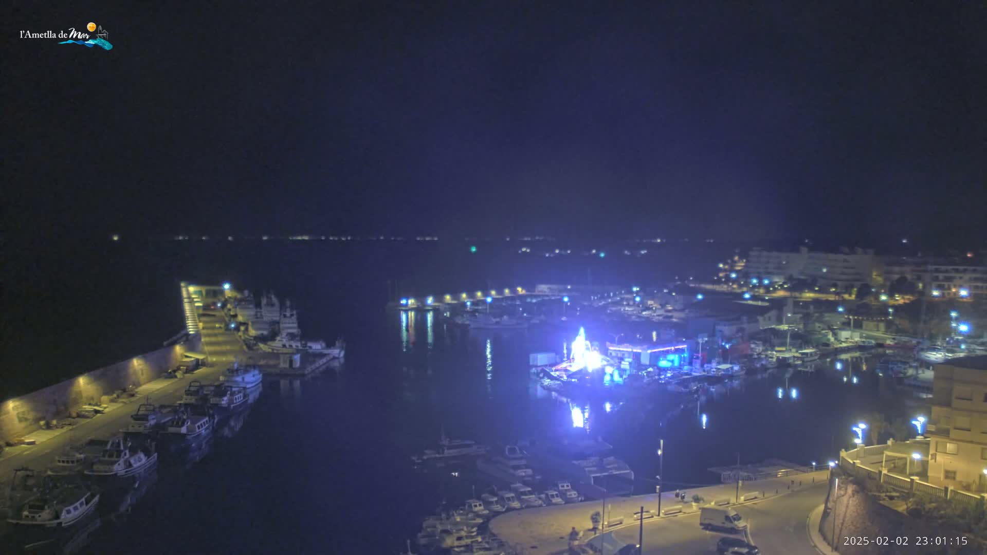 A nighttime aerial view of a harbor filled with boats, illuminated by lights, under a clear, dark sky.