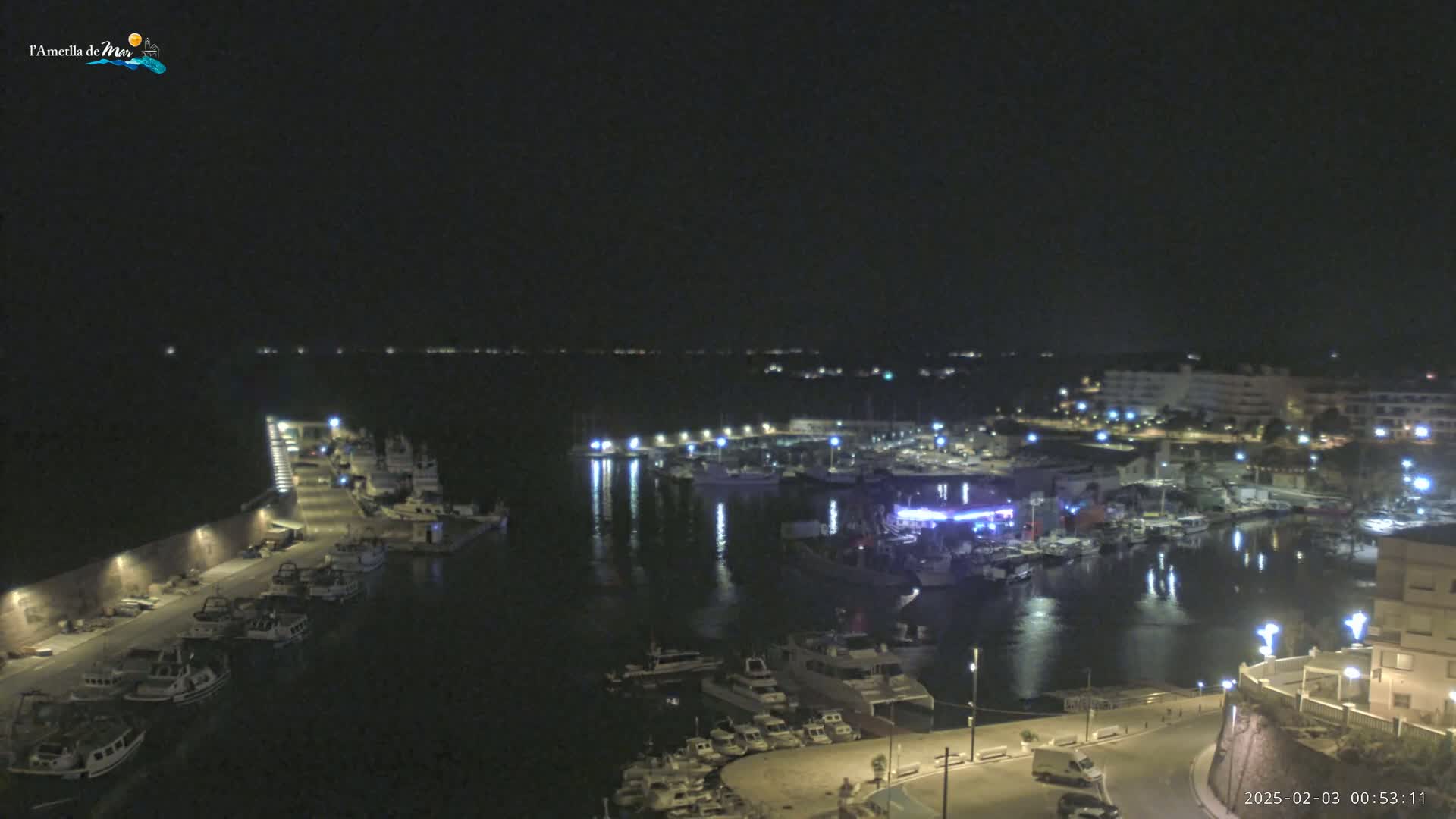 A nighttime view of a harbor filled with boats, illuminated by lights, under a clear, dark sky.