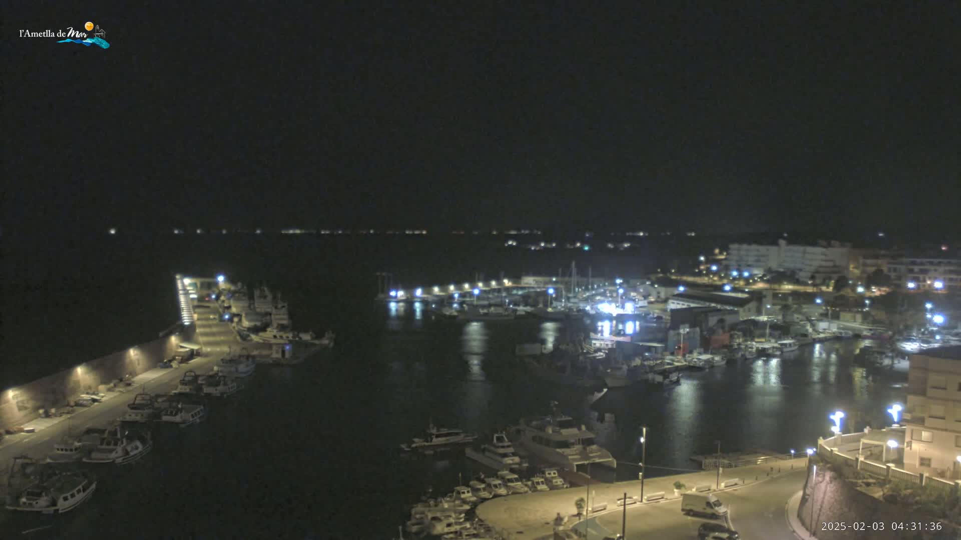 A nighttime aerial view of a harbor filled with boats and lit buildings, under a clear, dark sky.
