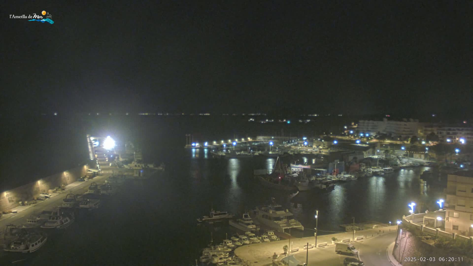 A nighttime, high-angle view of a harbor filled with boats, illuminated by lights along the docks and buildings surrounding the water.
