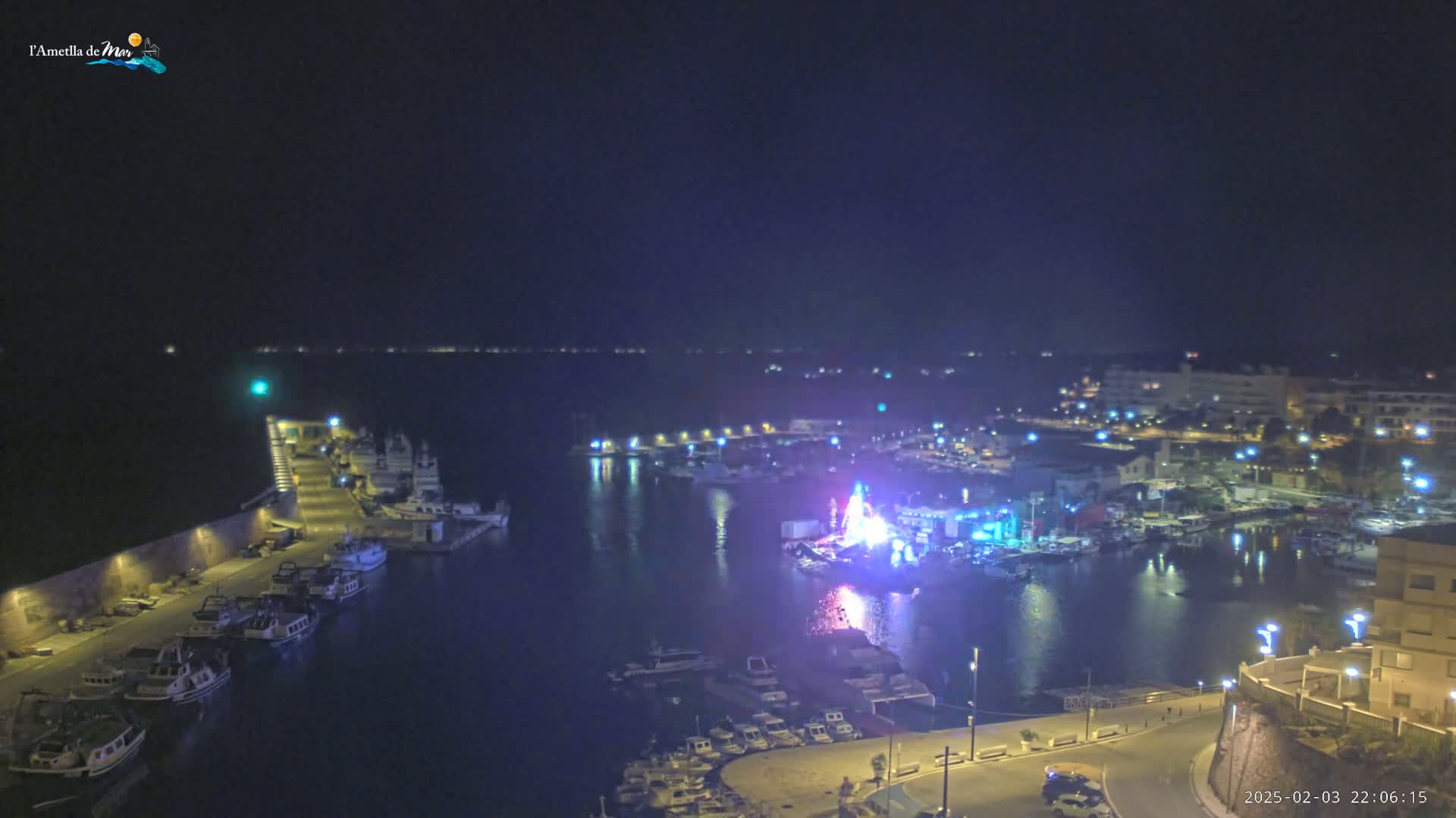 A nighttime aerial view of a harbor filled with boats, with a brightly lit display or event in the center of the harbor.