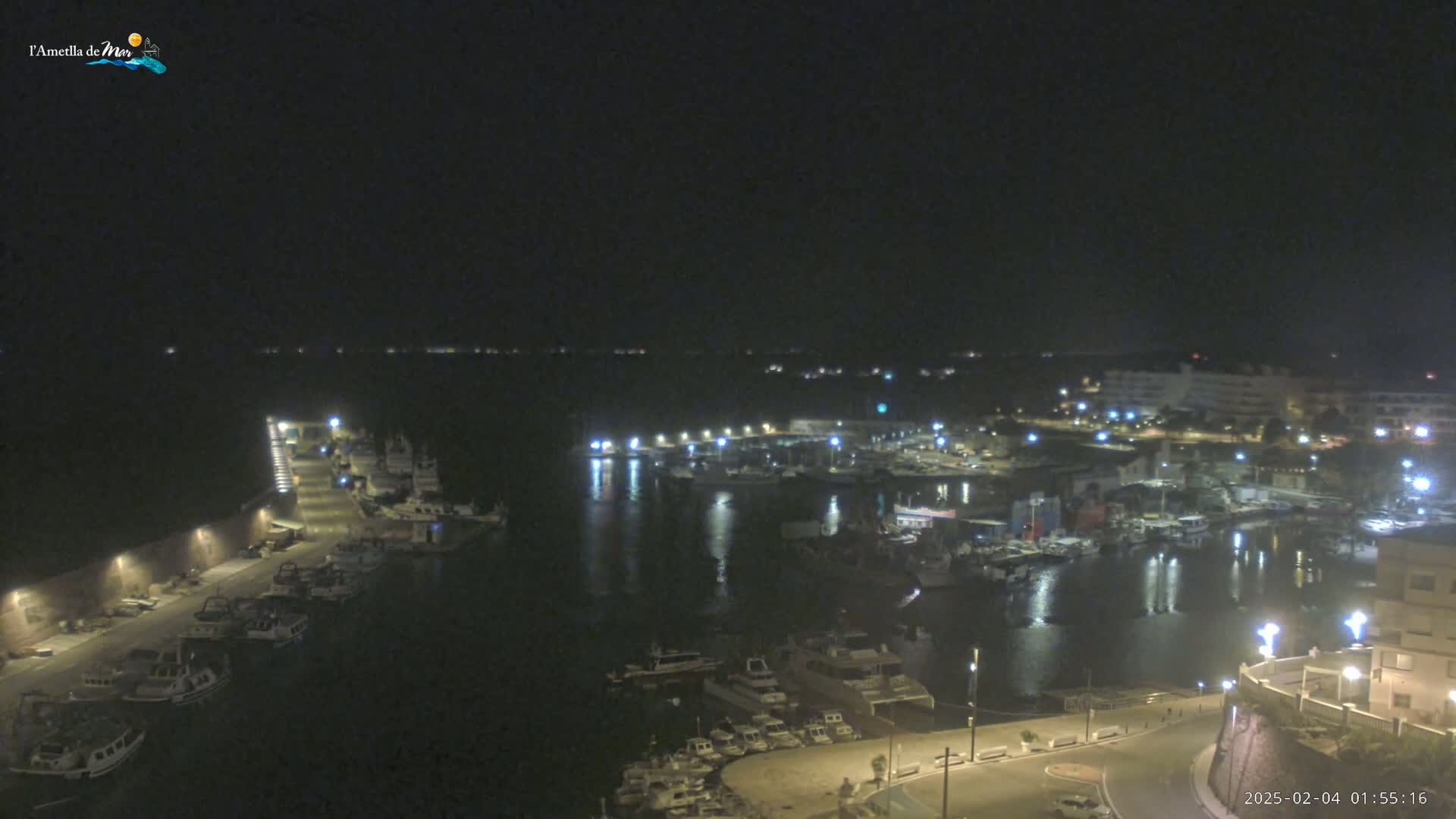 A nighttime view of a harbor filled with boats, illuminated by lights from the surrounding buildings and docks under a clear, dark sky.