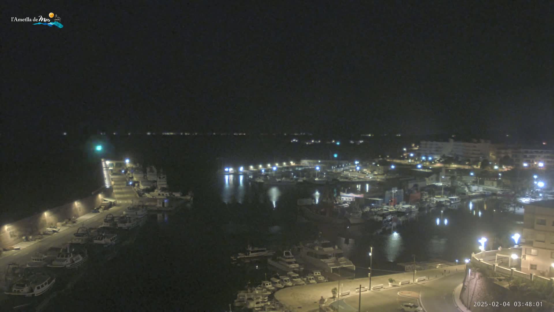 A nighttime, high-angle view of a harbor filled with boats, illuminated by lights along the docks and buildings on the shore.